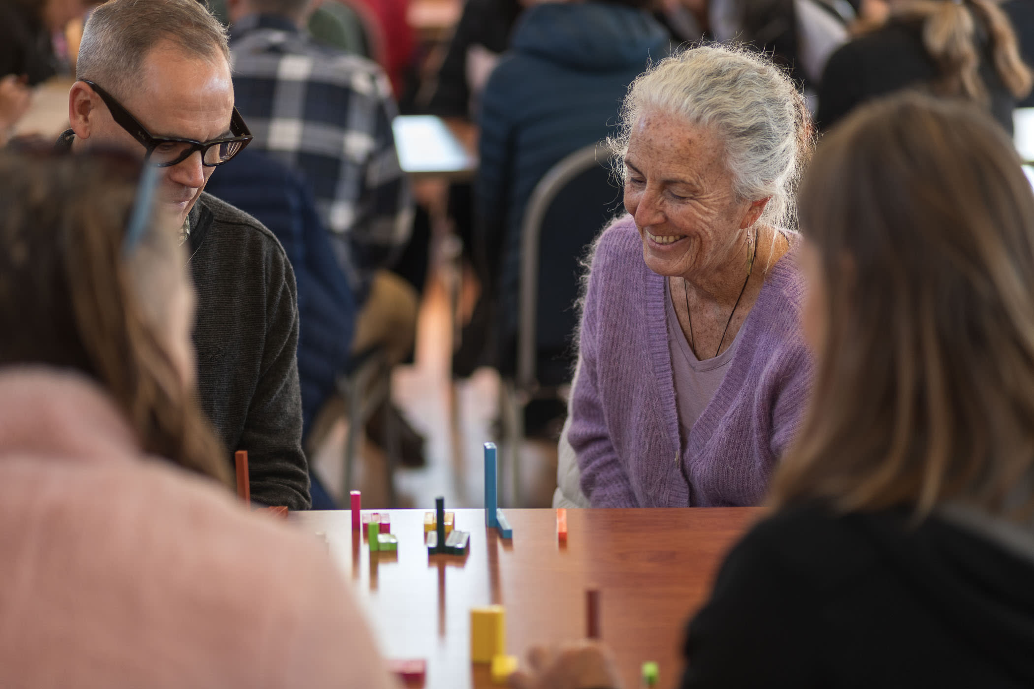 two people sitting at a table smiling, looking at cuisinaire rods