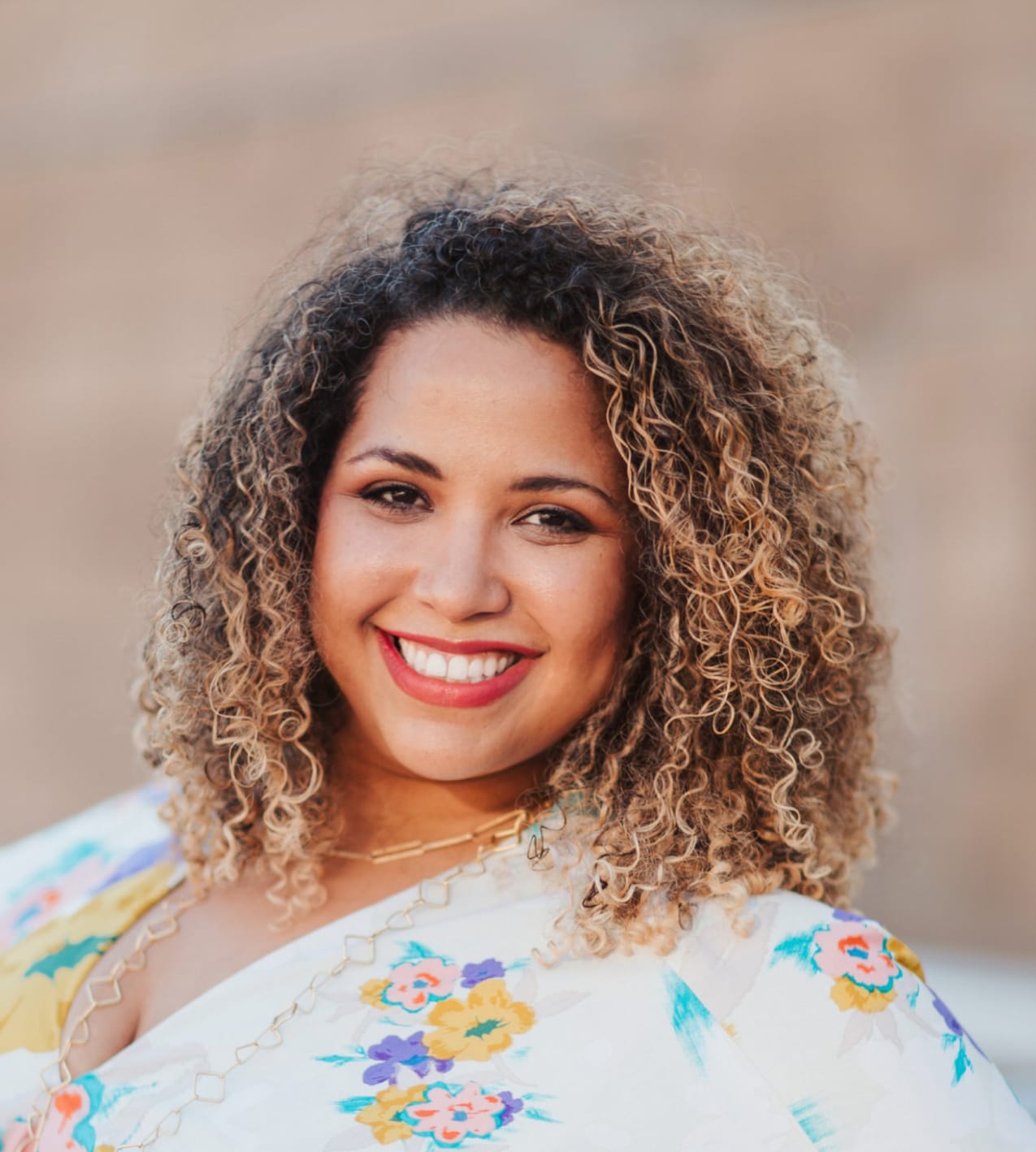 Afro-latina smiling with Curly hair and a floral dress.