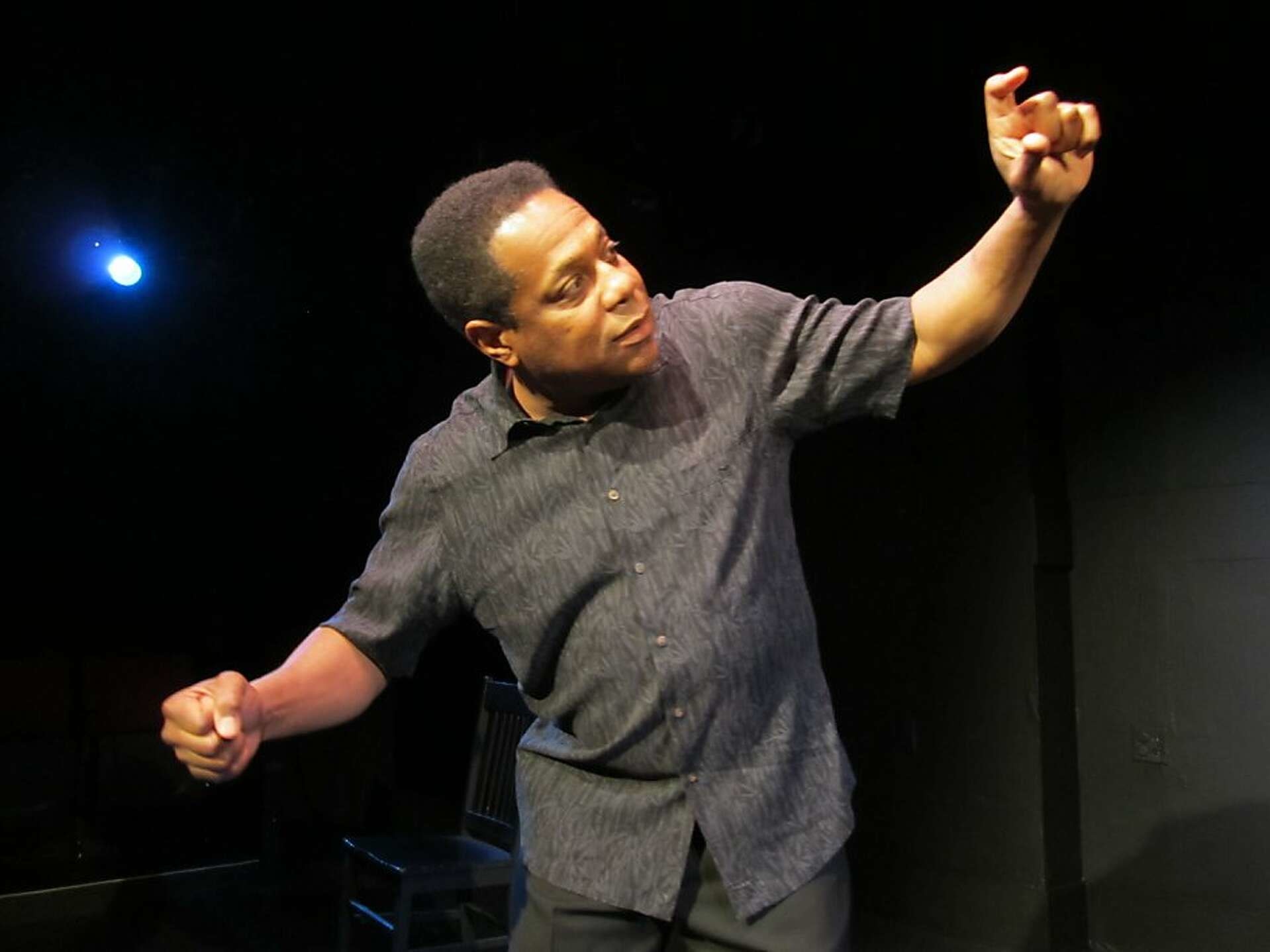 Brian Copeland with arms outstretched, wearing a gray shirt, in a blackbox theater