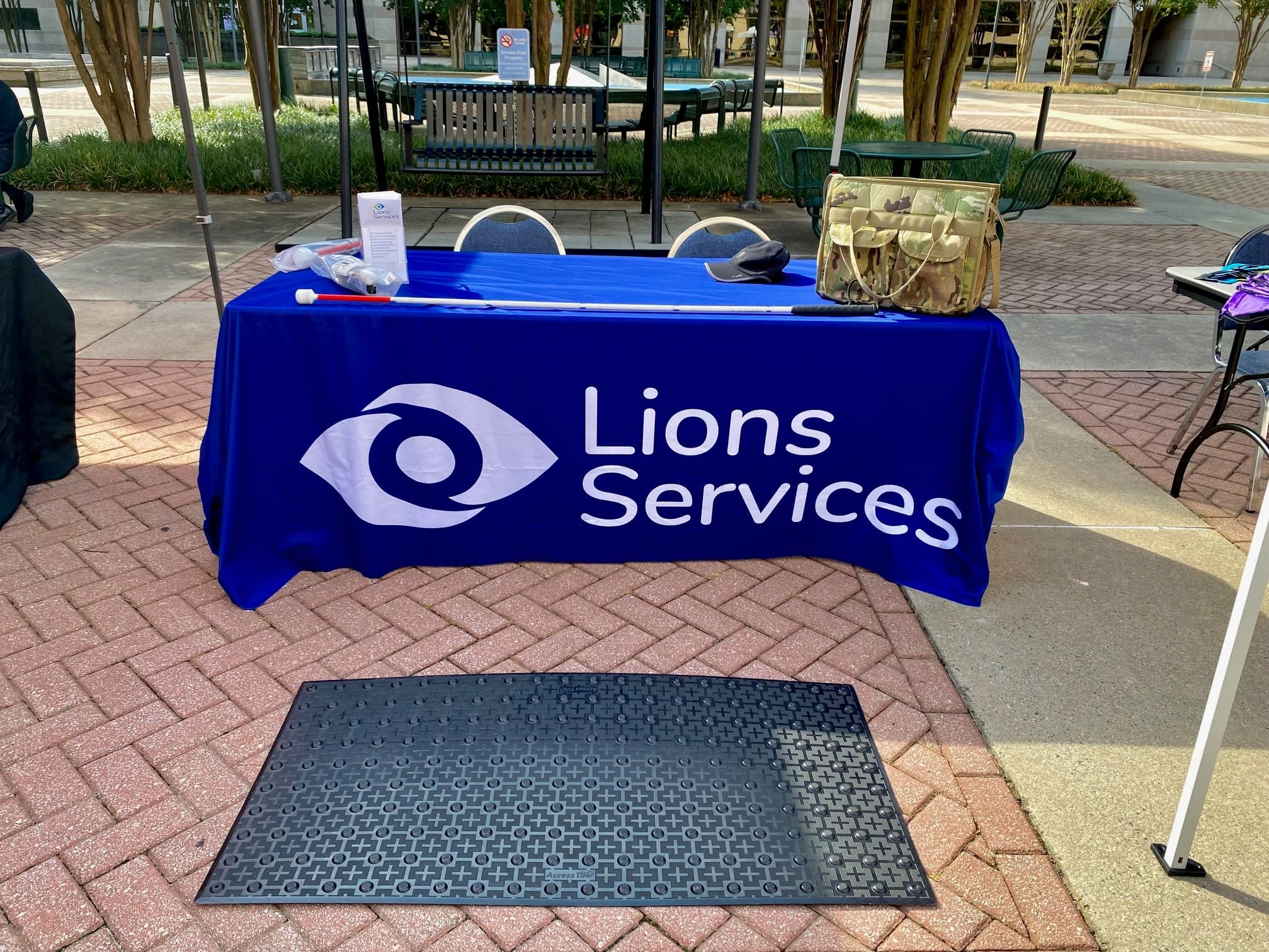 able with a blue and white table cloth with the Lions Services logo and a long white cane, Lions brochures on display.