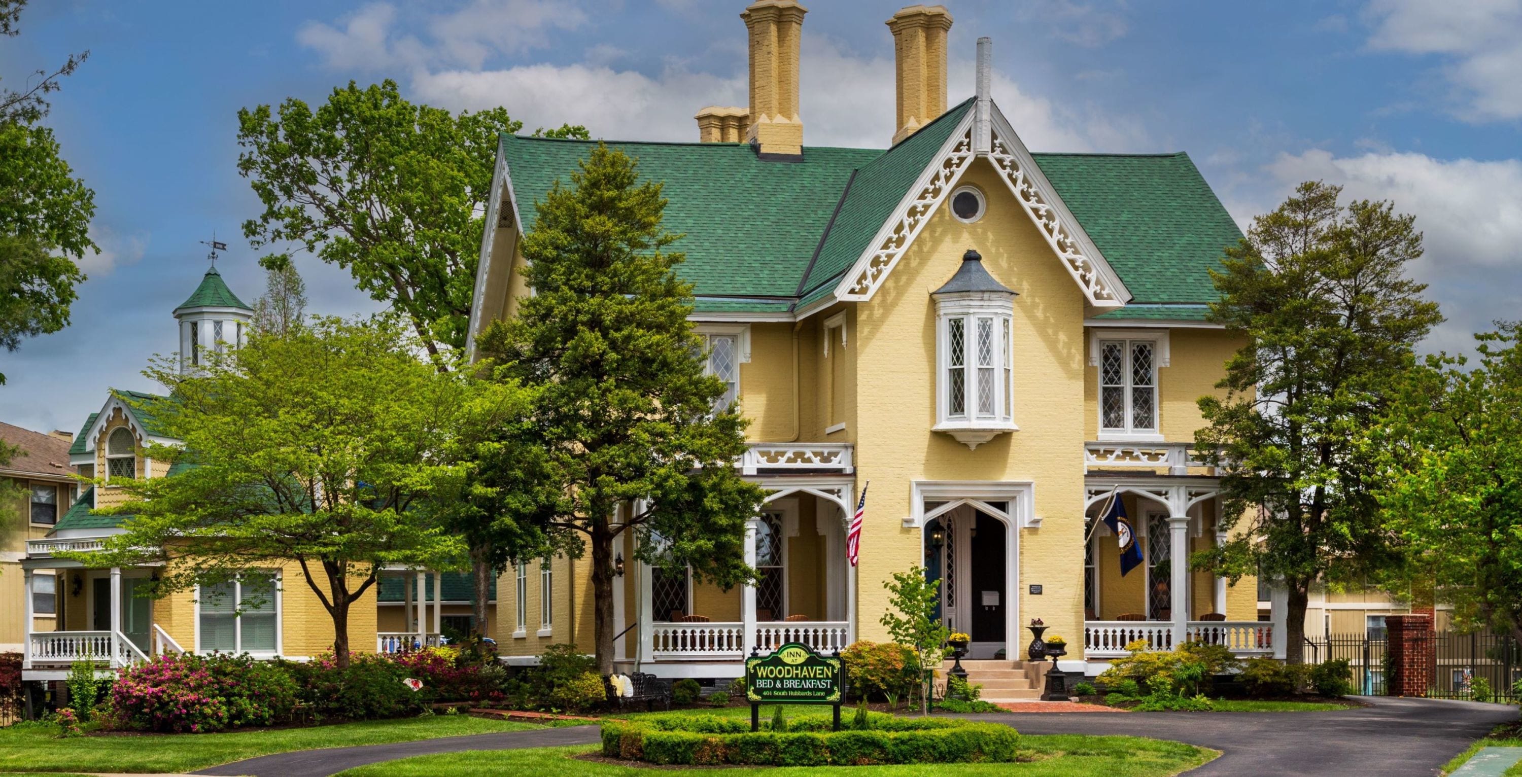 street view of yellow three story gothic mansion with white gingerbreading and a green shingled roof.