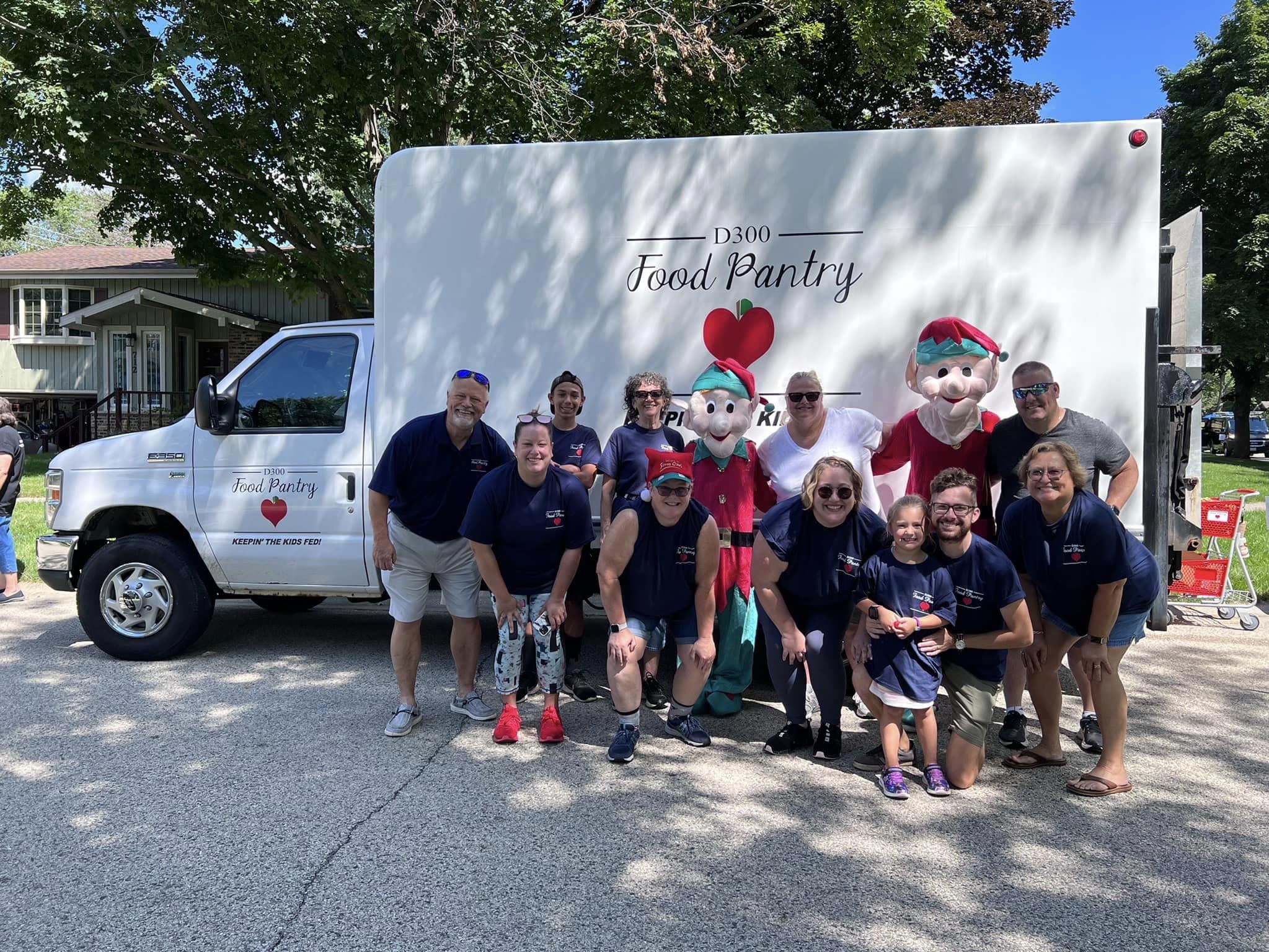 a large group of people and two in elf costumes in front of a white box truck with the D300 Food Pantry logo on the side