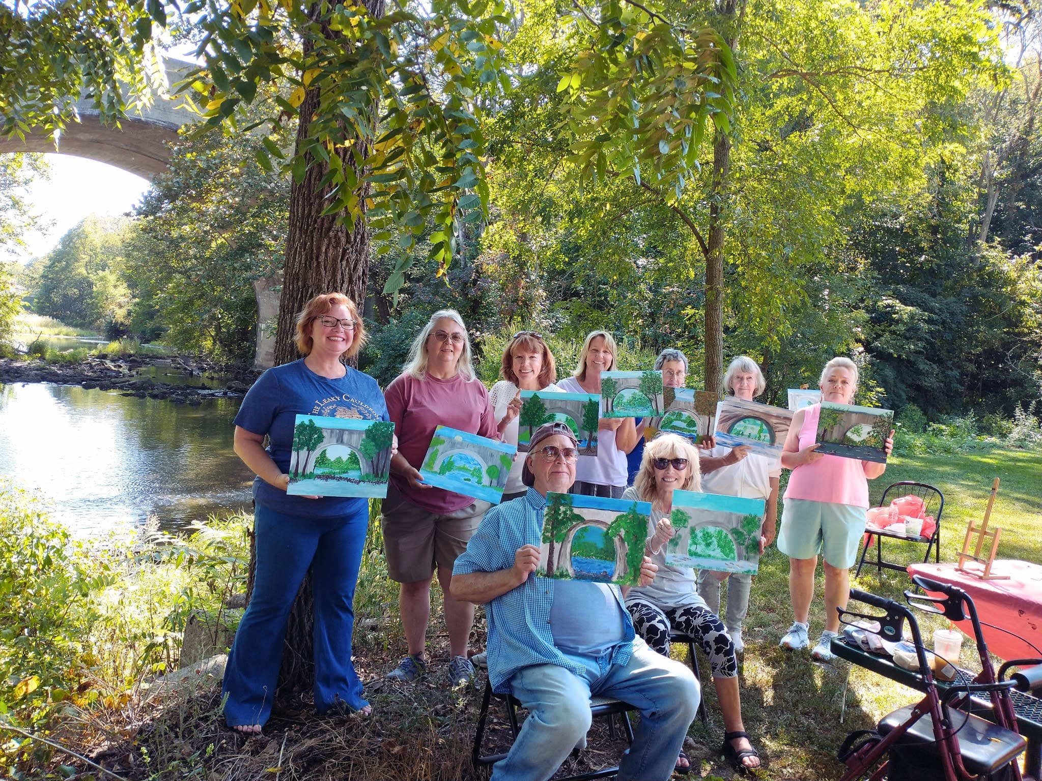 A group of impressive painters holding up their finished artwork at an outdoor park.