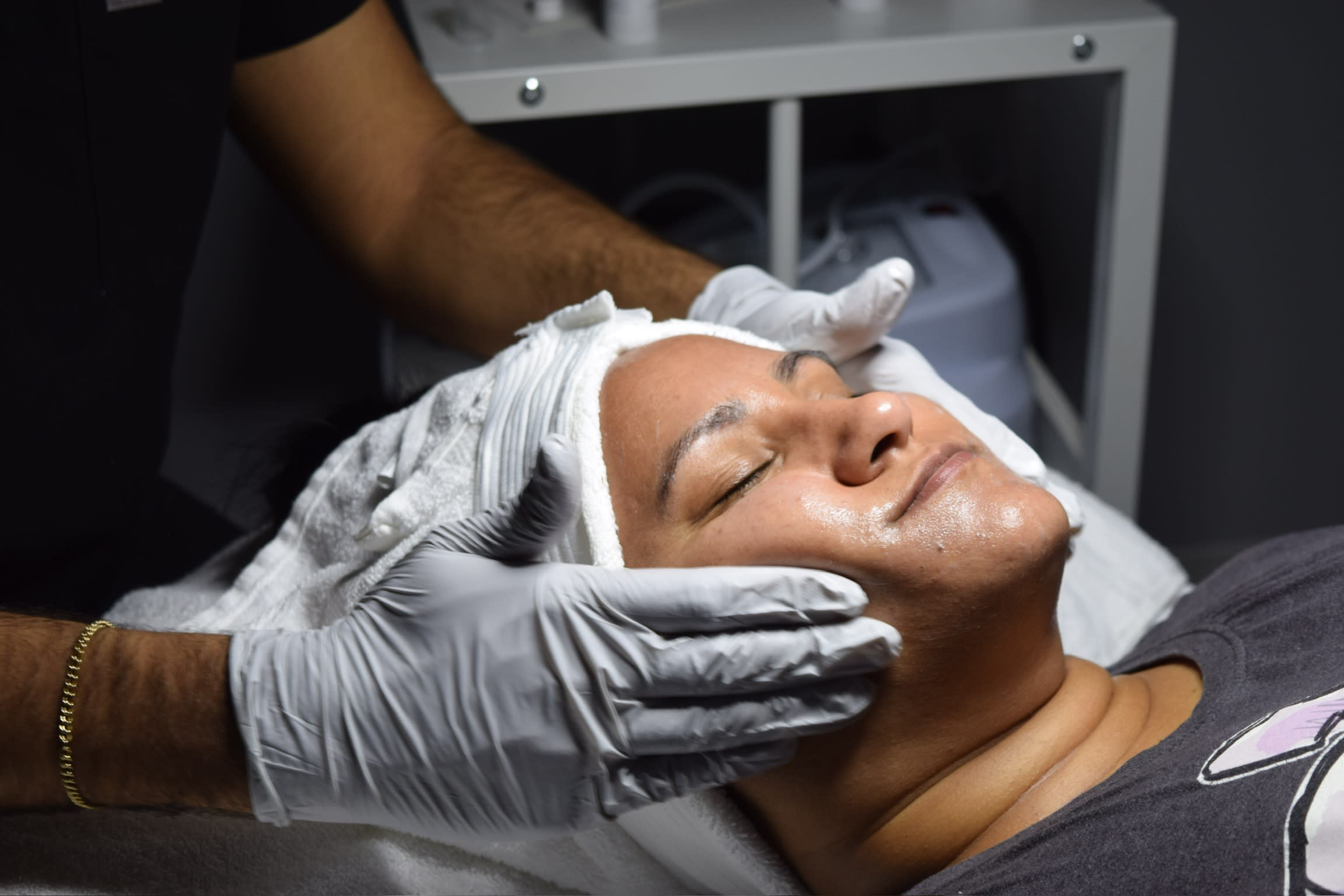 Woman receiving a facial treatment at a medical spa, lying down with eyes closed as an aesthetician applies skincare products