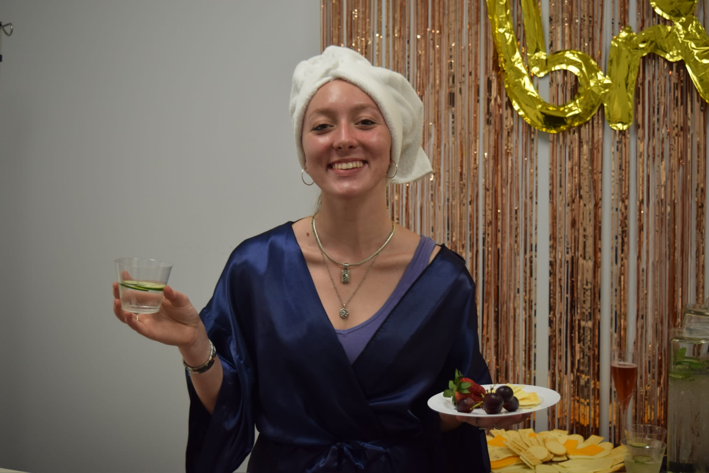 Woman standing, holding a plate of appetizers in one hand and a drink in the other, smiling and enjoying the spa.