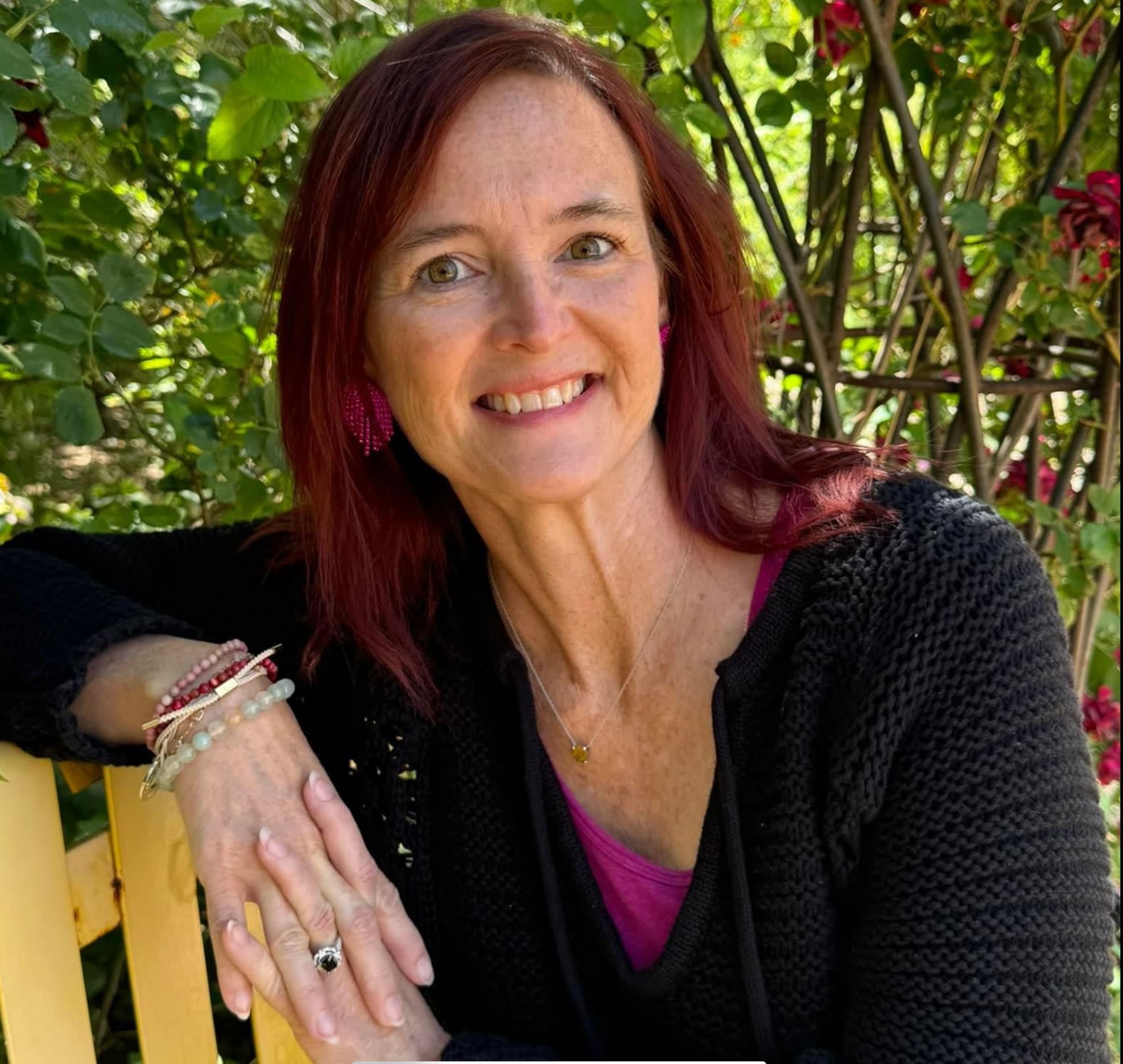 Early 50’s white woman with red hair wearing a black sweater and several bracelets