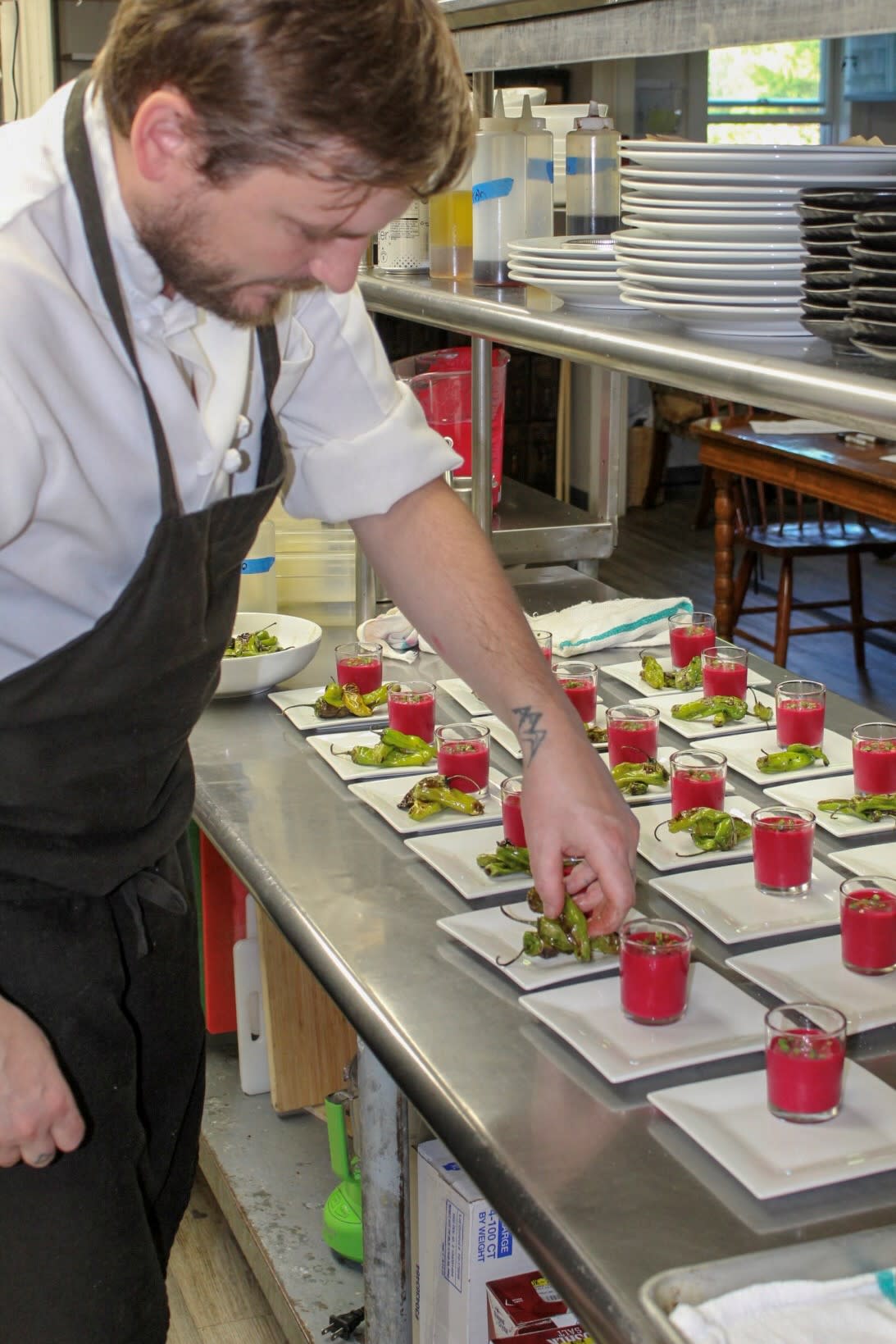 Chef preparing plates of chilled beet soup shots paired with blackened shishito peppers for an event