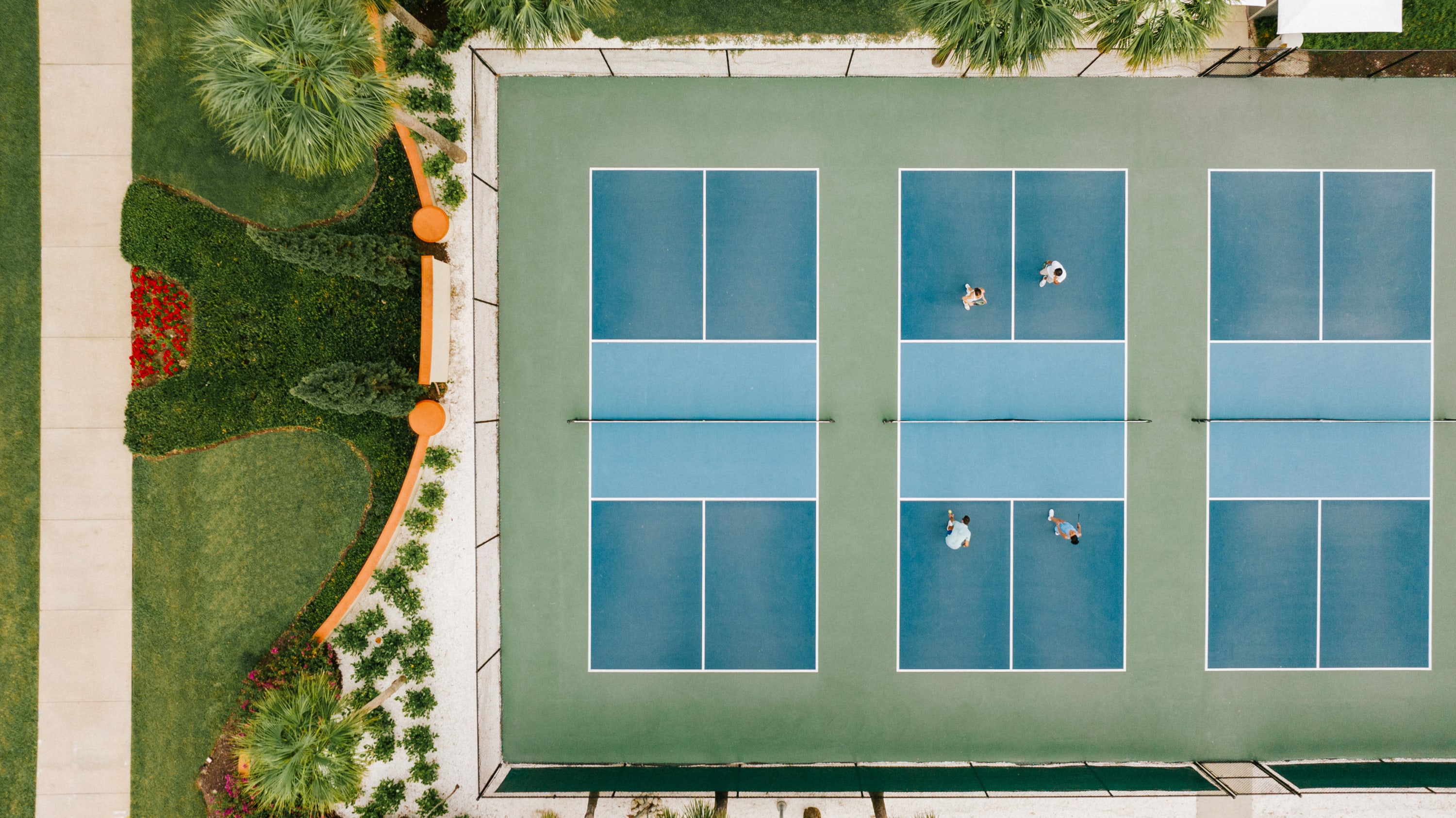 Overhead aerial of three pickleball courts next to manicured landscape