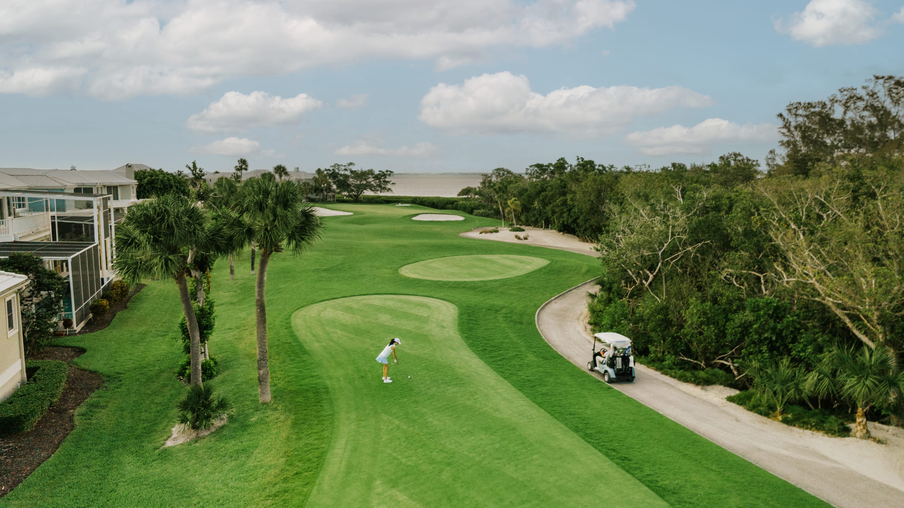 Woman on golf course with cart on the path between houses and woods