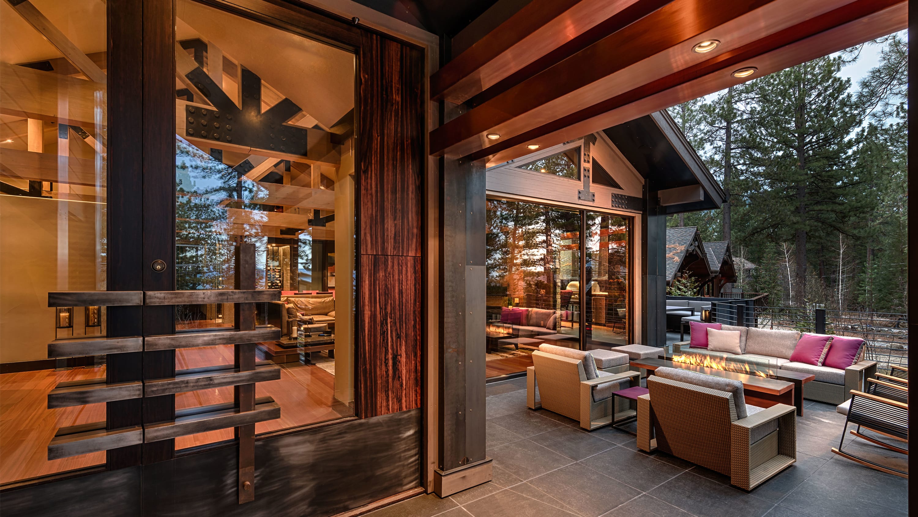Exteiror of a mountain home, seating area with fire pit, large doors and windows into the home