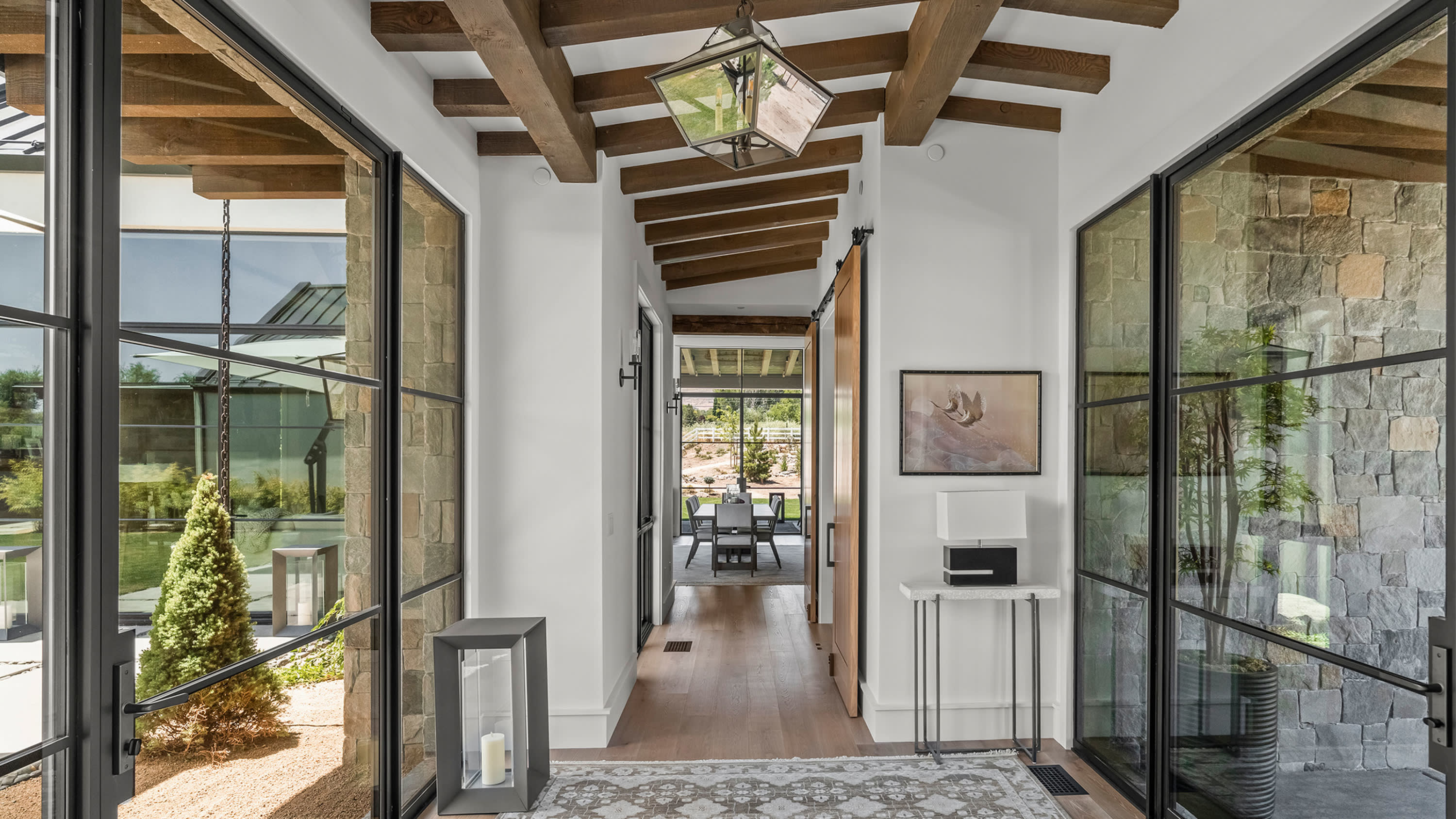 Hallway with exposed wood beams, glass walls, and stone elements in a modern custom home