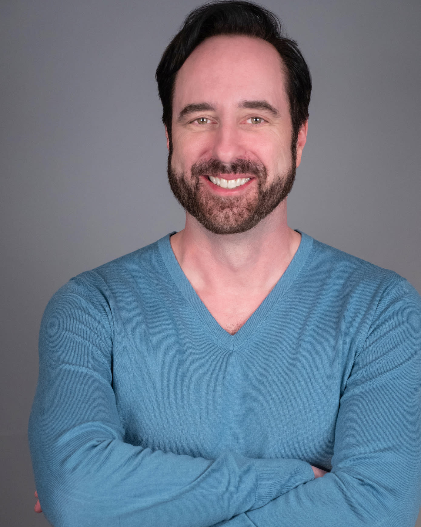 Bill Connington, a white man in a blue sweater with dark brown hair and beard, smiles to the camera with arms crossed