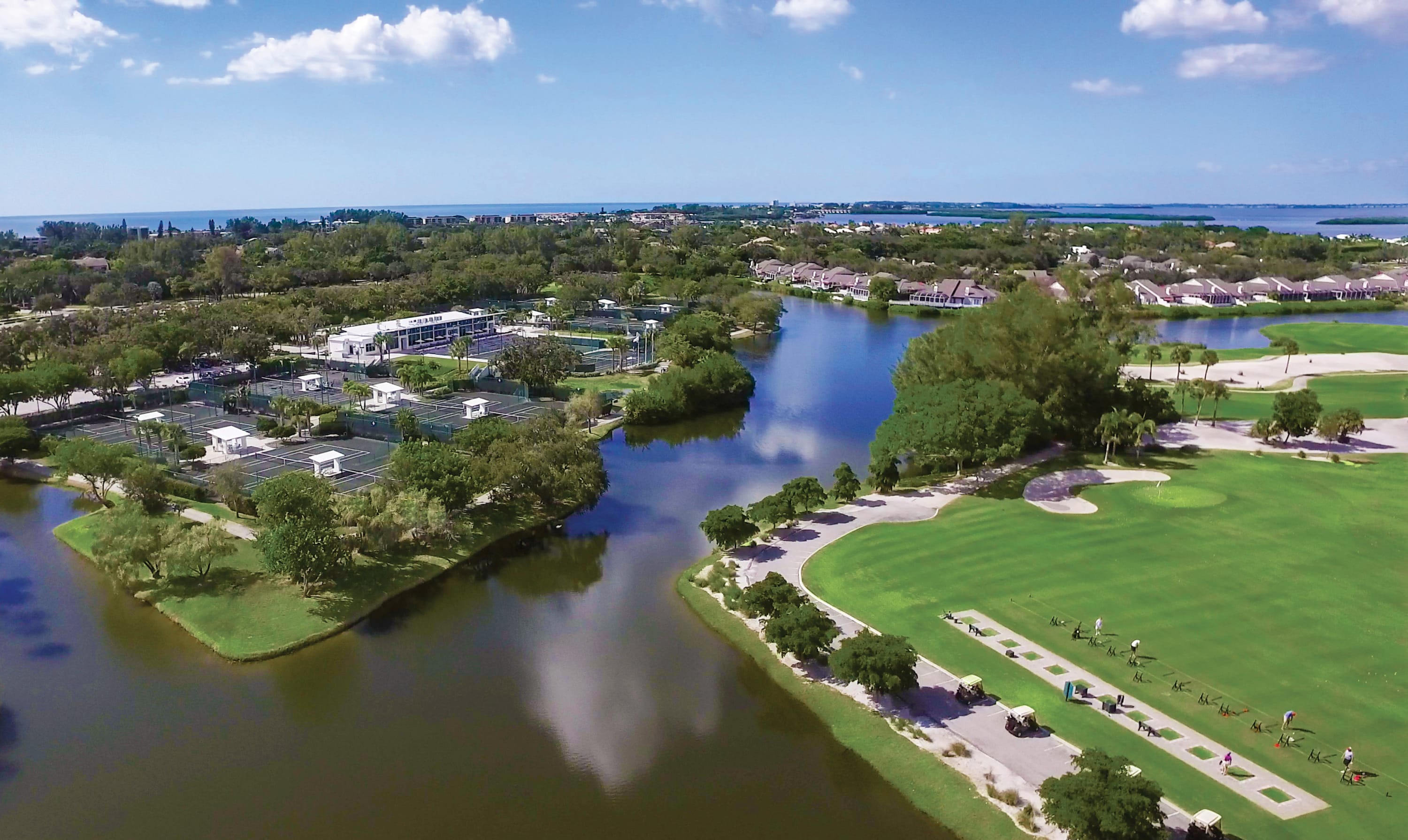 Tennis courts and golf driving range separated by lagoon water with blue sky above