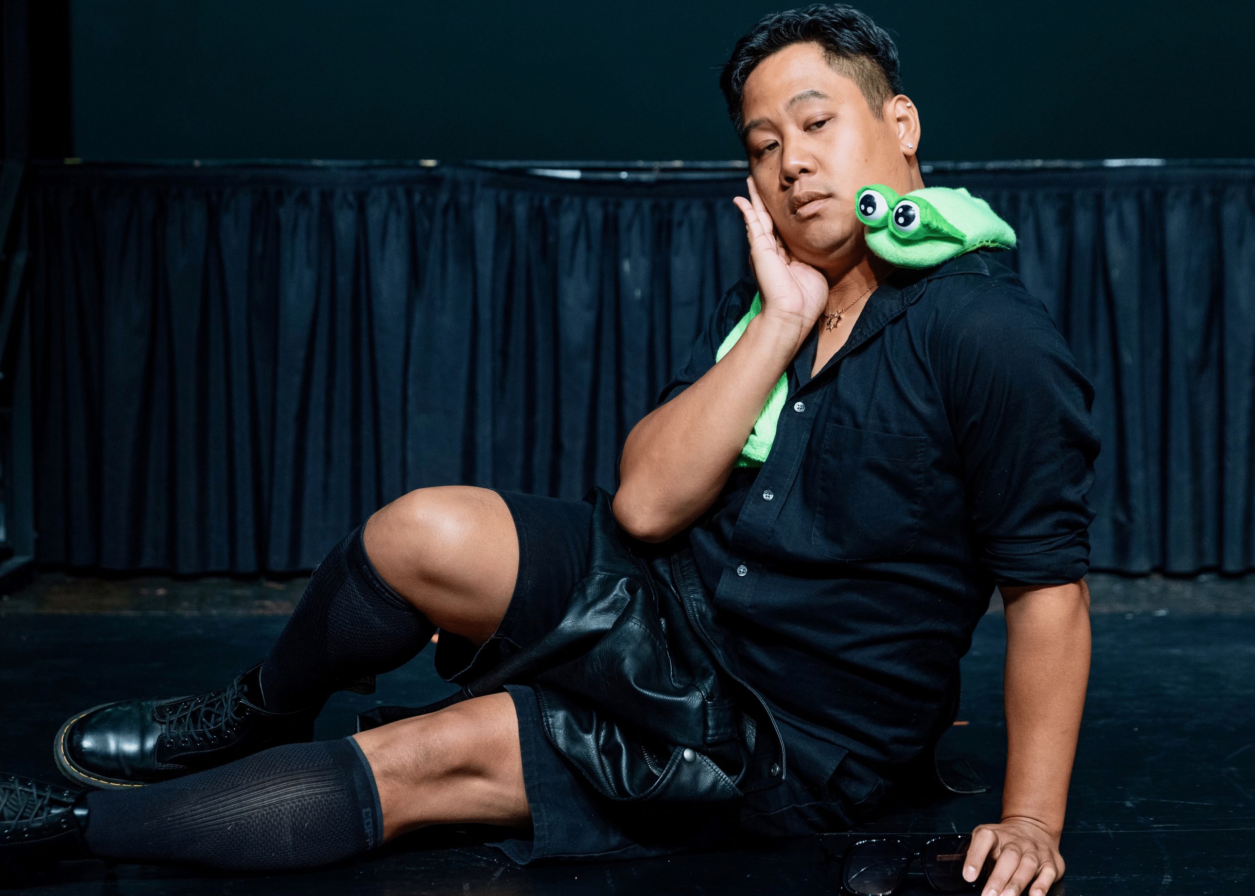 actor leaning seductively with a green eel puppet draped around their shoulders