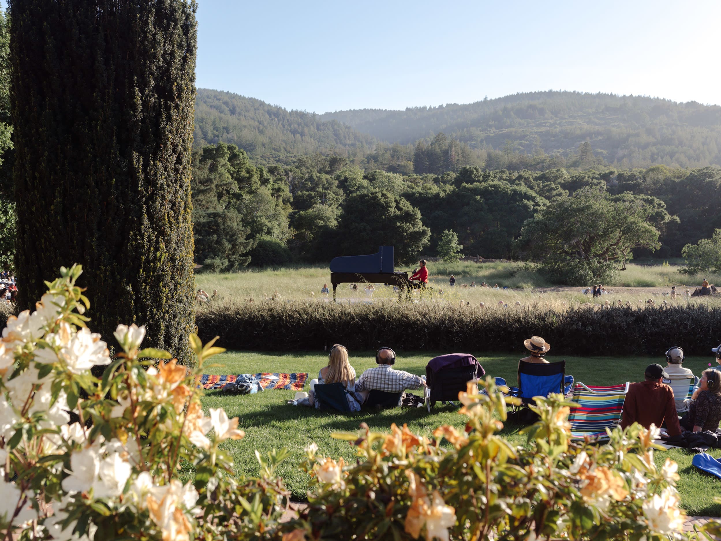 Hunter Noack plays piano in a green meadow surrounded by audience members sitting and standing a short distance from the pian