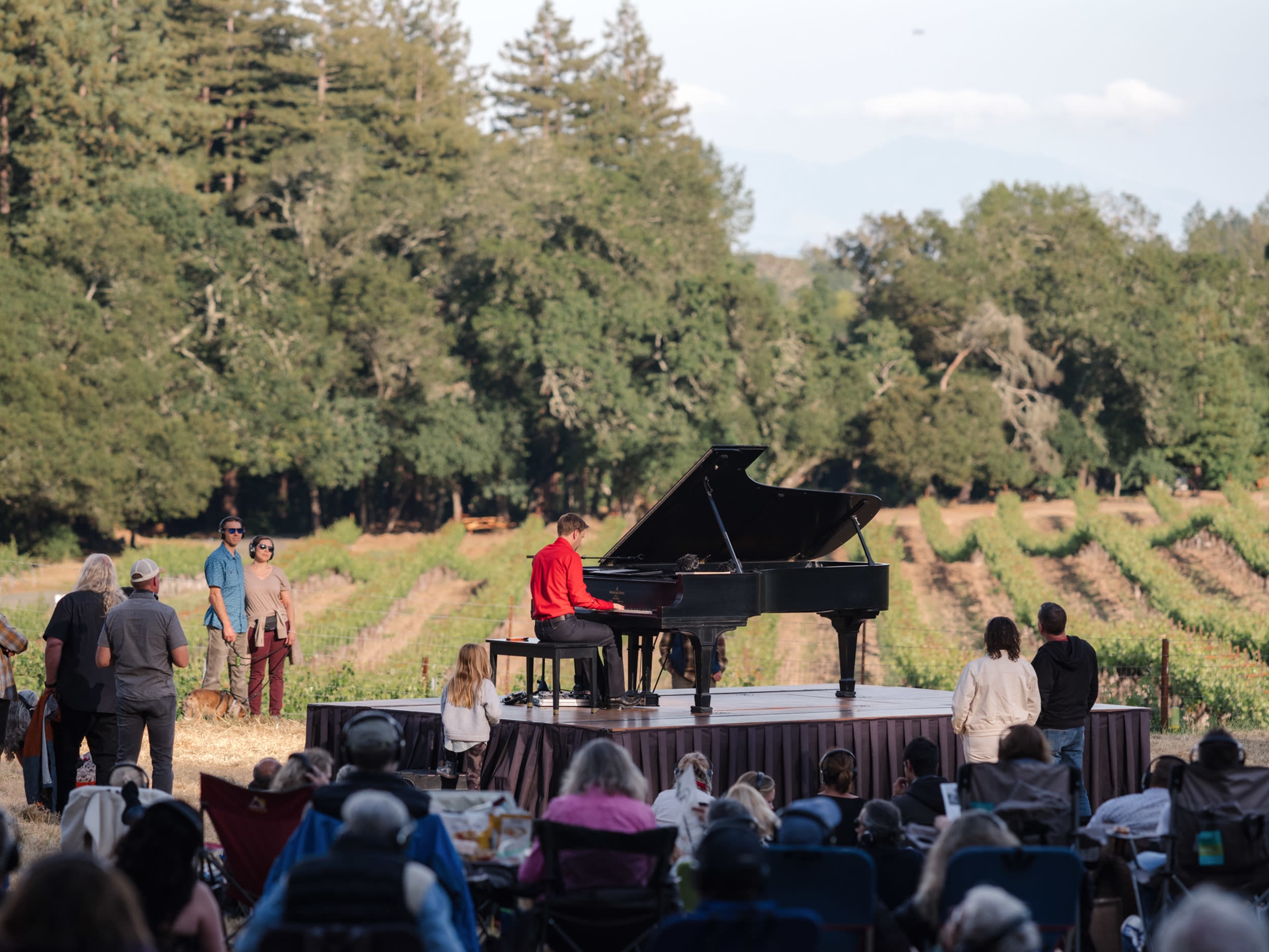 Hunter Noack plays piano surrounded by audience members seated in camp chairs, on the ground or walking around