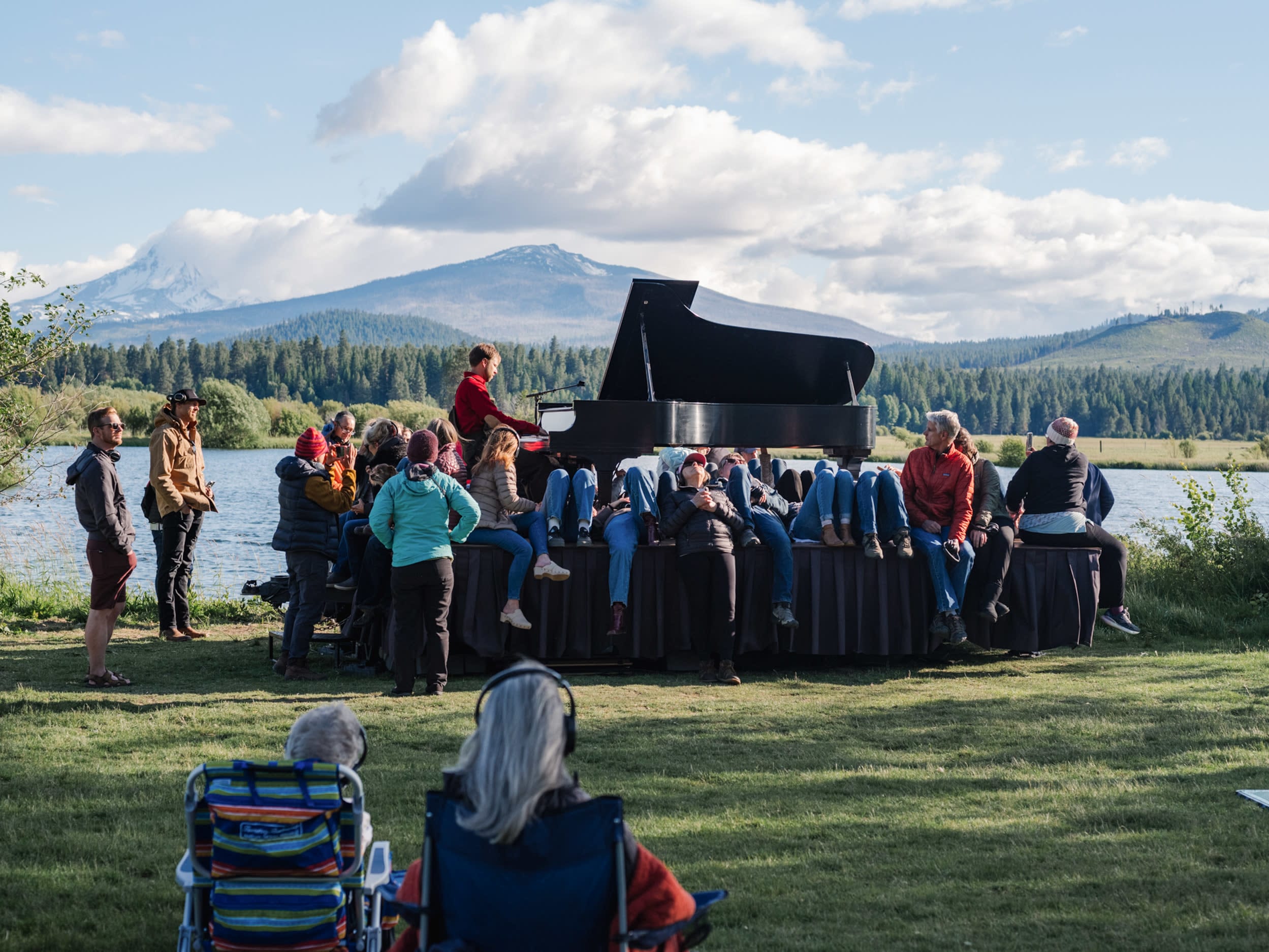 Hunter Noack plays a piano on a trailer. Audience members surround him and the piano while others are seated in chairs. The