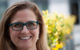 smiling woman wearing glasses with a yellow plant blurred in the background