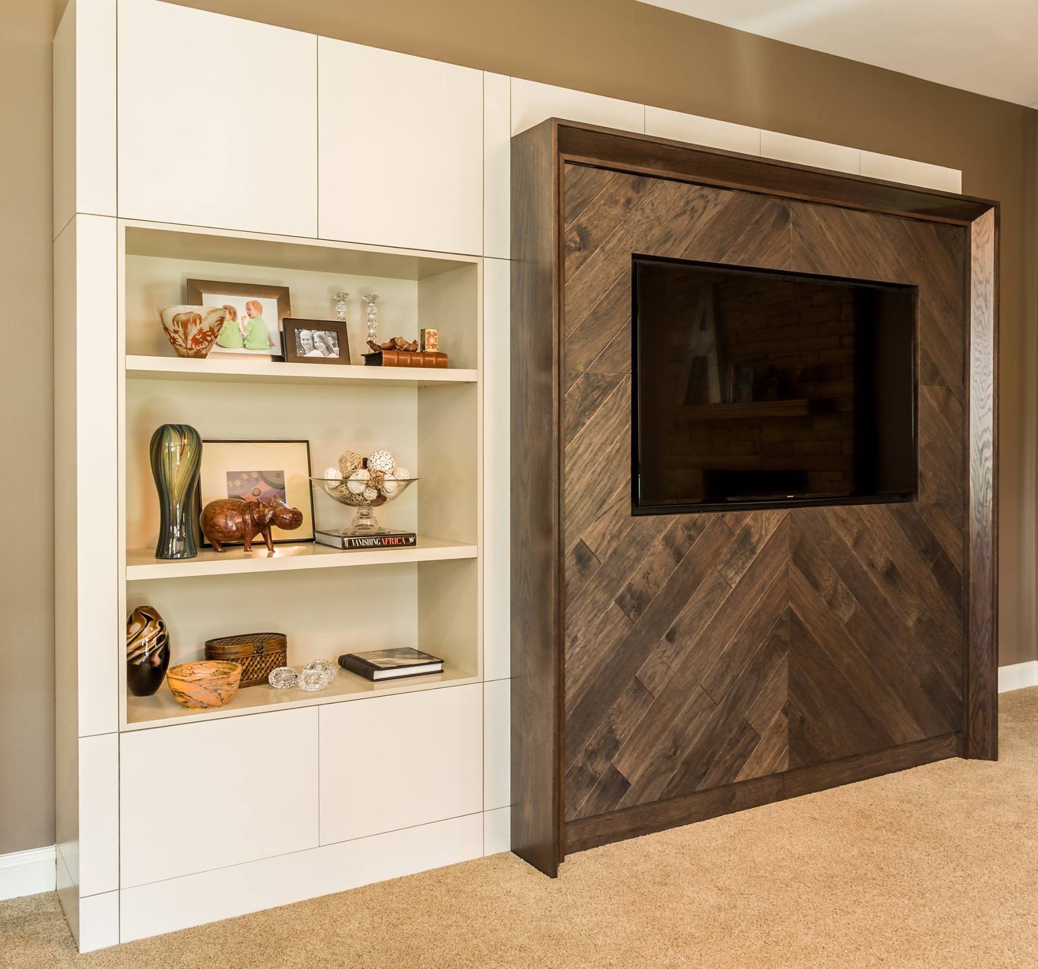 A modern custom wall unit featuring white built-in bookshelves with various decorative items, and a dark wood Murphy bed cab