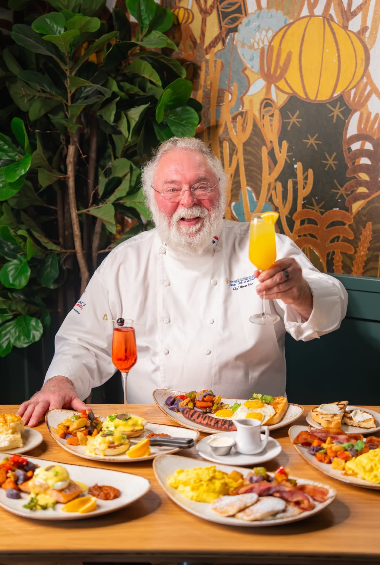 Chef Mercer Mohr raising a mimosa while seated at a table of brunch dishes at Rascal Modern Diner in Sedona.