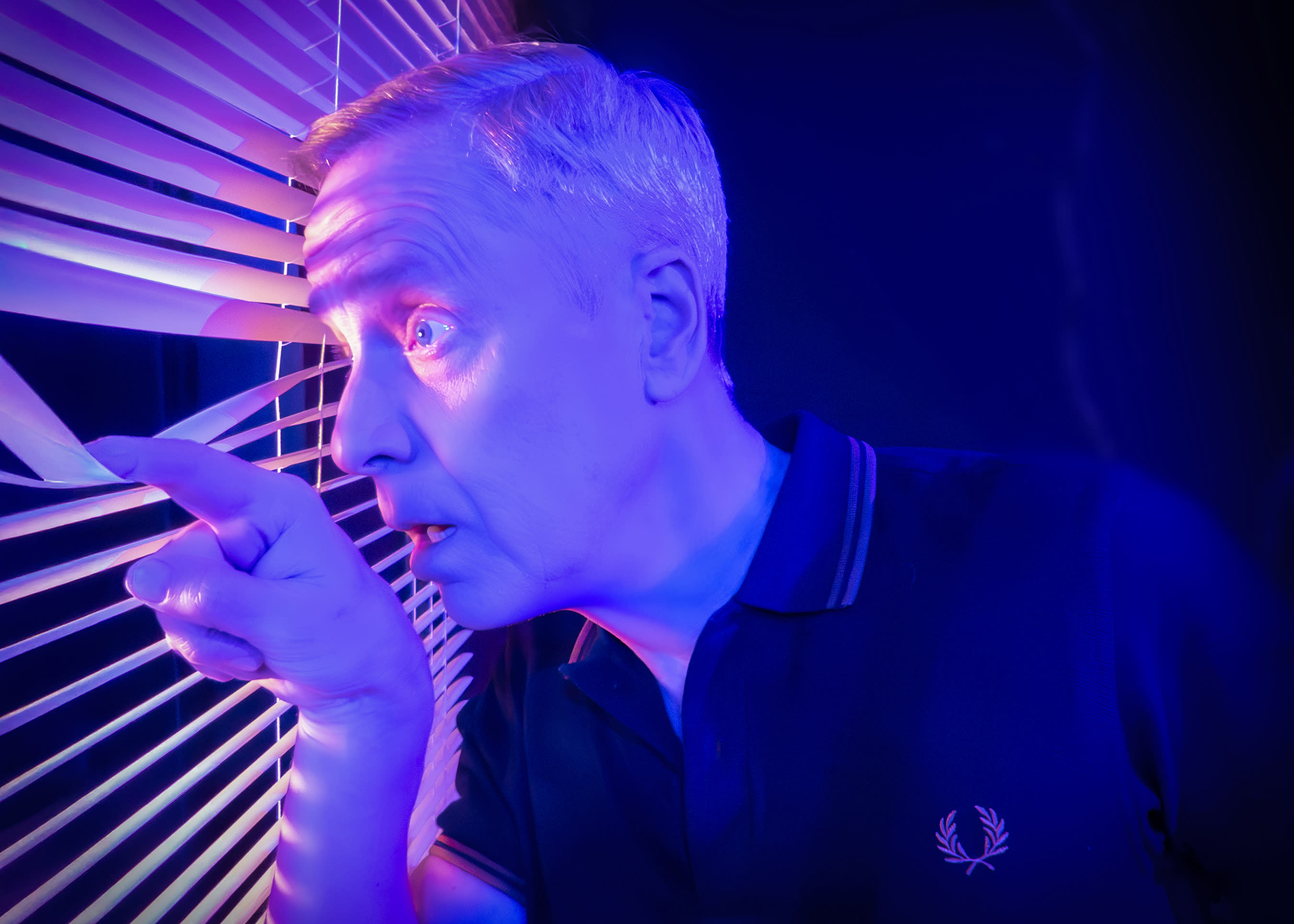 Performer looking through window blind looking scared.