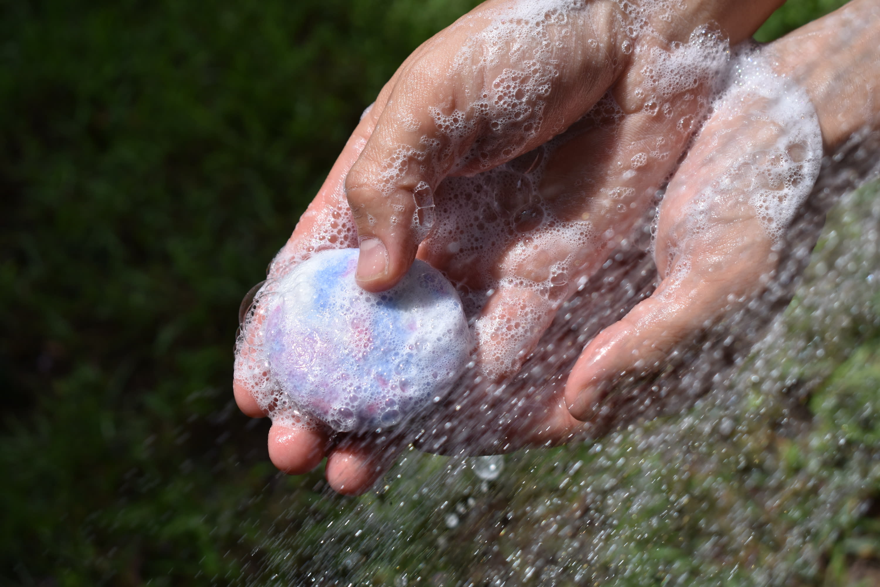 Hands holding a Tangie shampoo bar under running water as it lathers with bubbly foam.