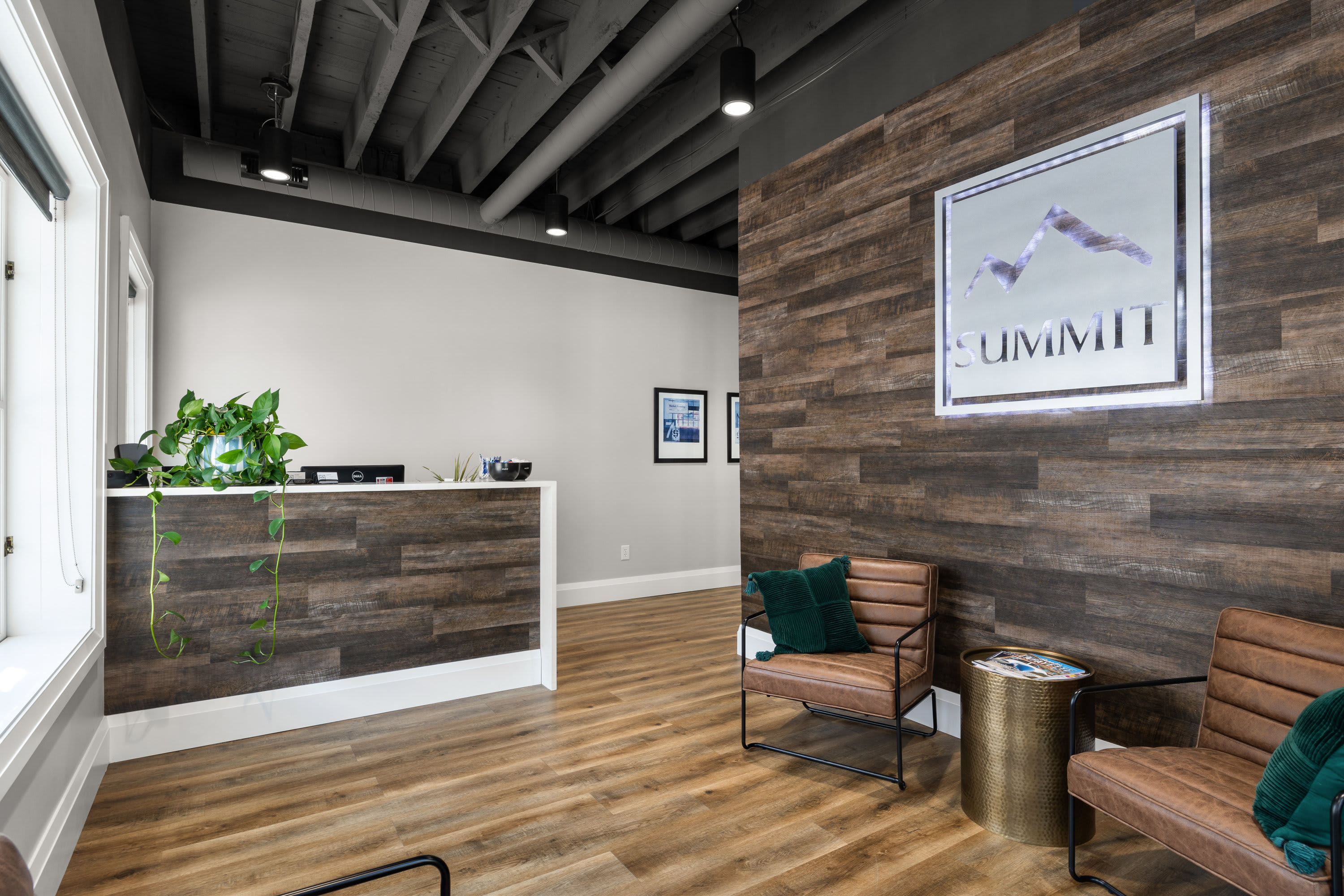 Modern office lobby of Summit with a reception desk, plant, brown leather chairs with green pillow