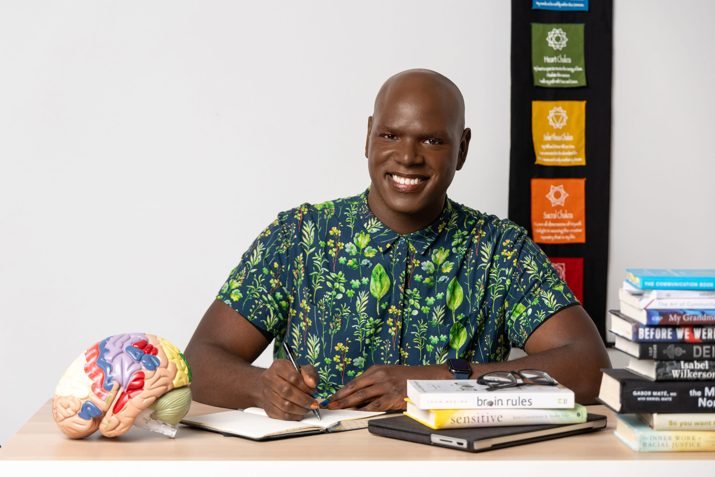 Chris D. Hooten sitting at a desk writing in their notebook while smiling