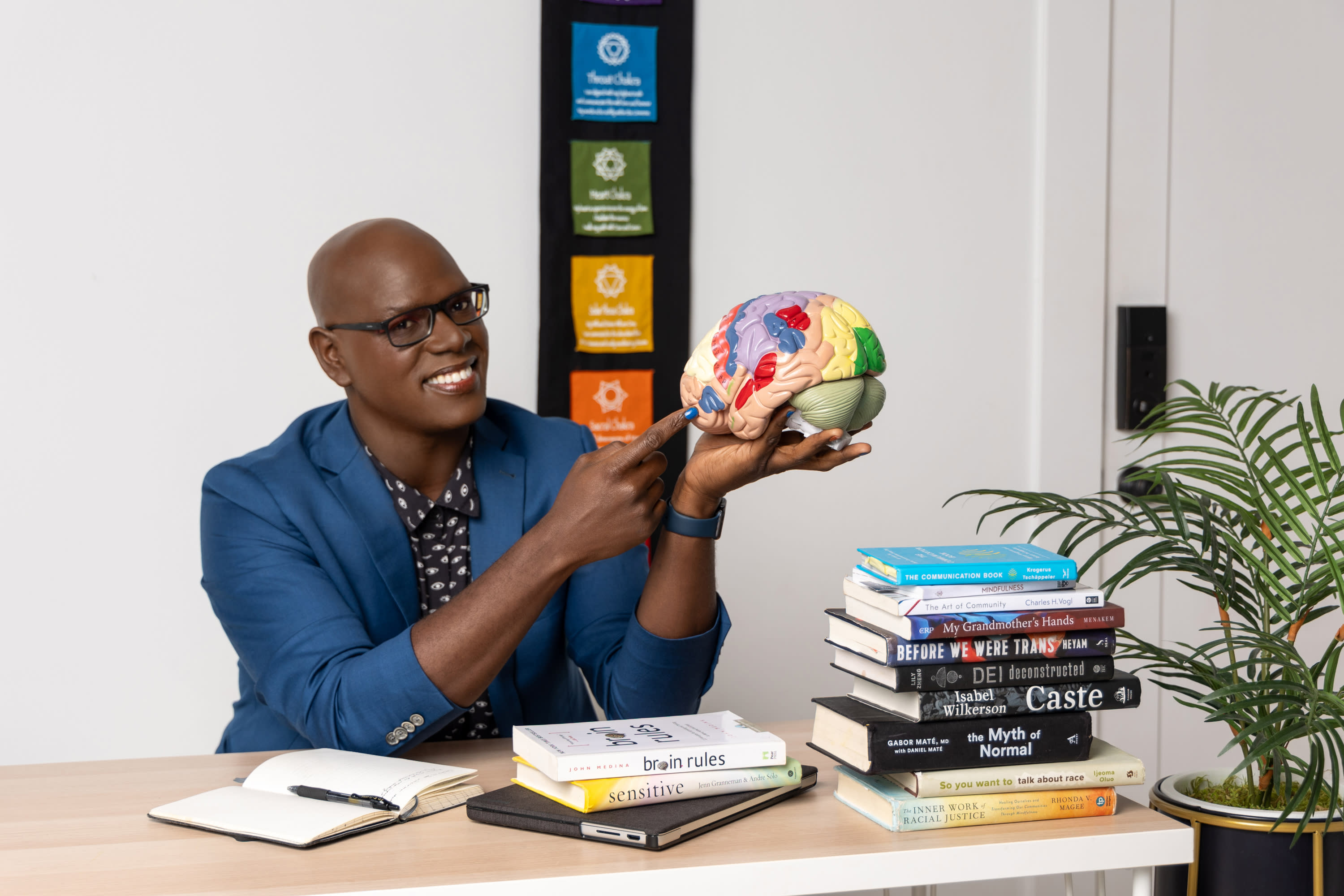 Chris D. Hooten sitting at a desk pointing to a 3-D model of a human brain while smiling