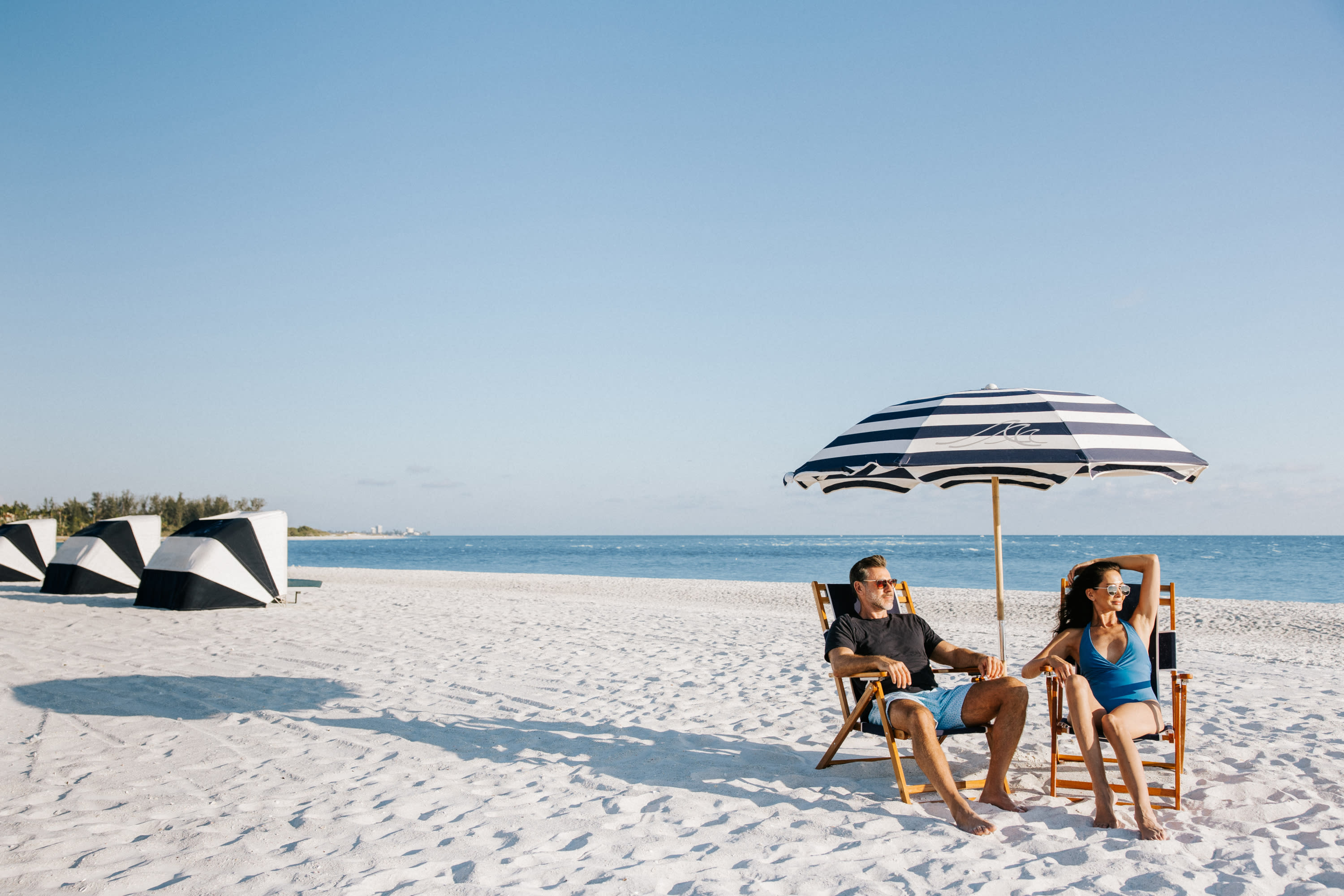White sand beach with cabanas and a man and woman sitting under and umbrella overlooking the Gulf