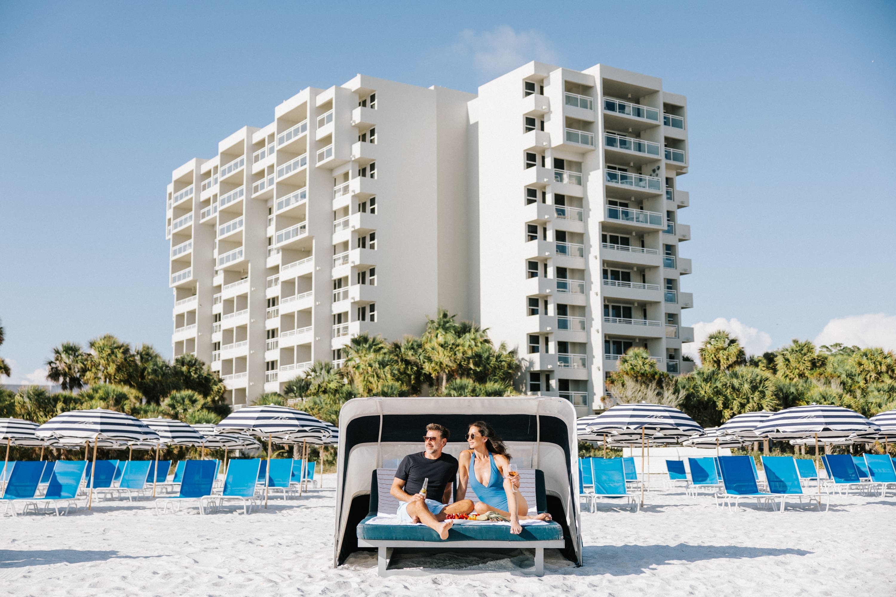 Couple in a beach cabana in front of many beach chairs with umbrellas and The Resort building in the background