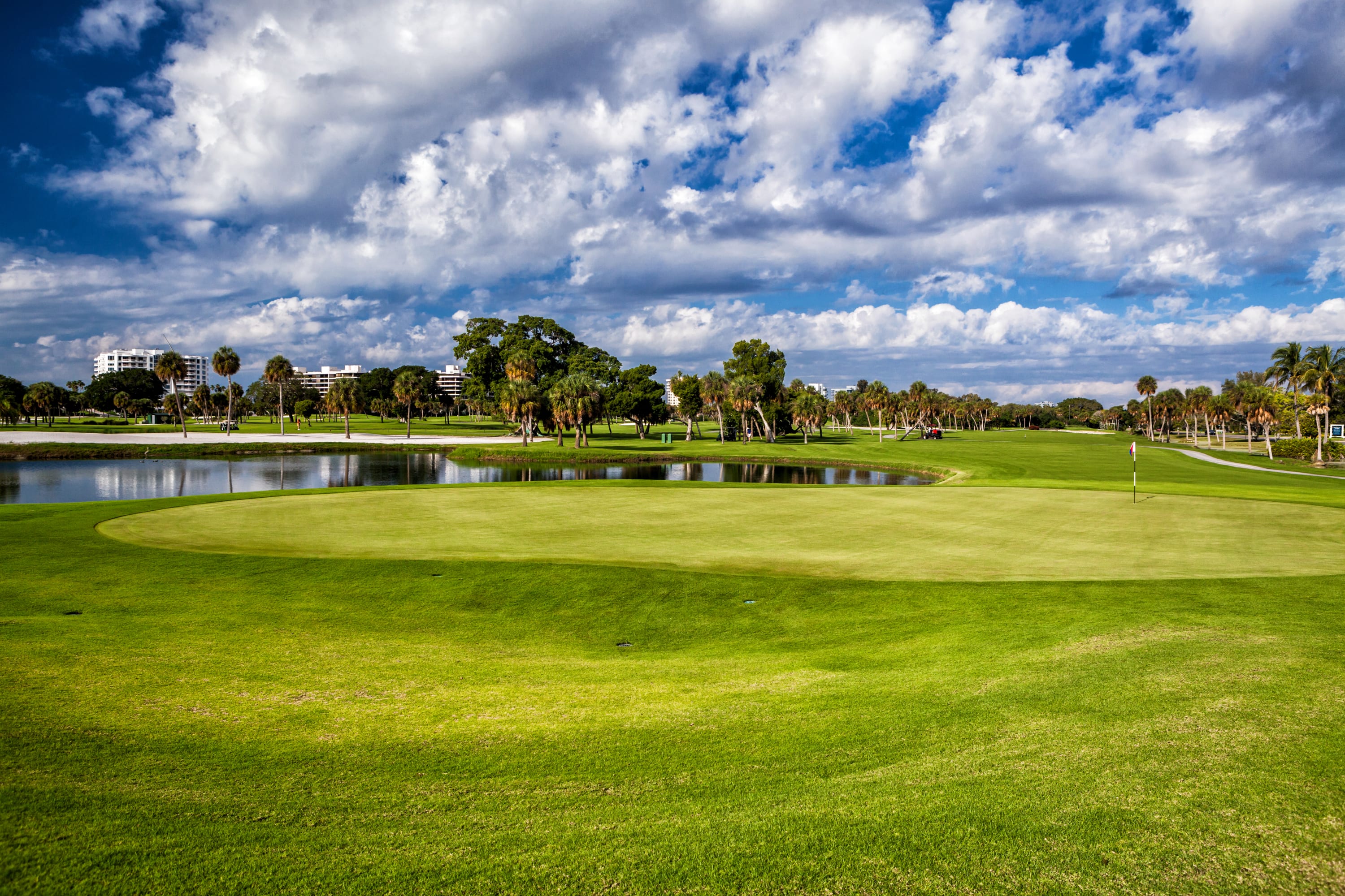 Golf fairway next to pond with condos and cloudy blue sky in the background