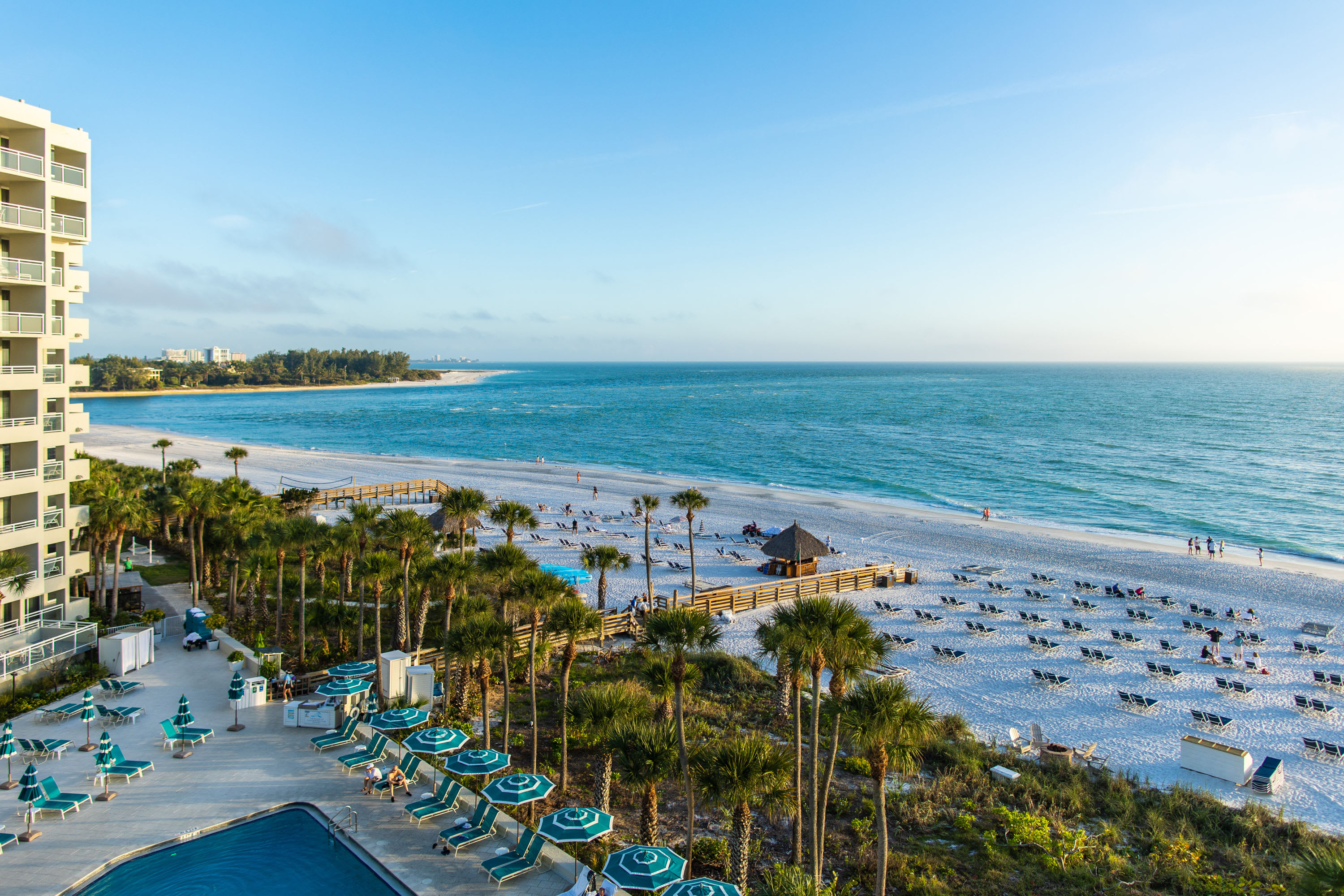 Resort building and pool with beach chairs and umbrellas overlooking the beach filled with beach chairs