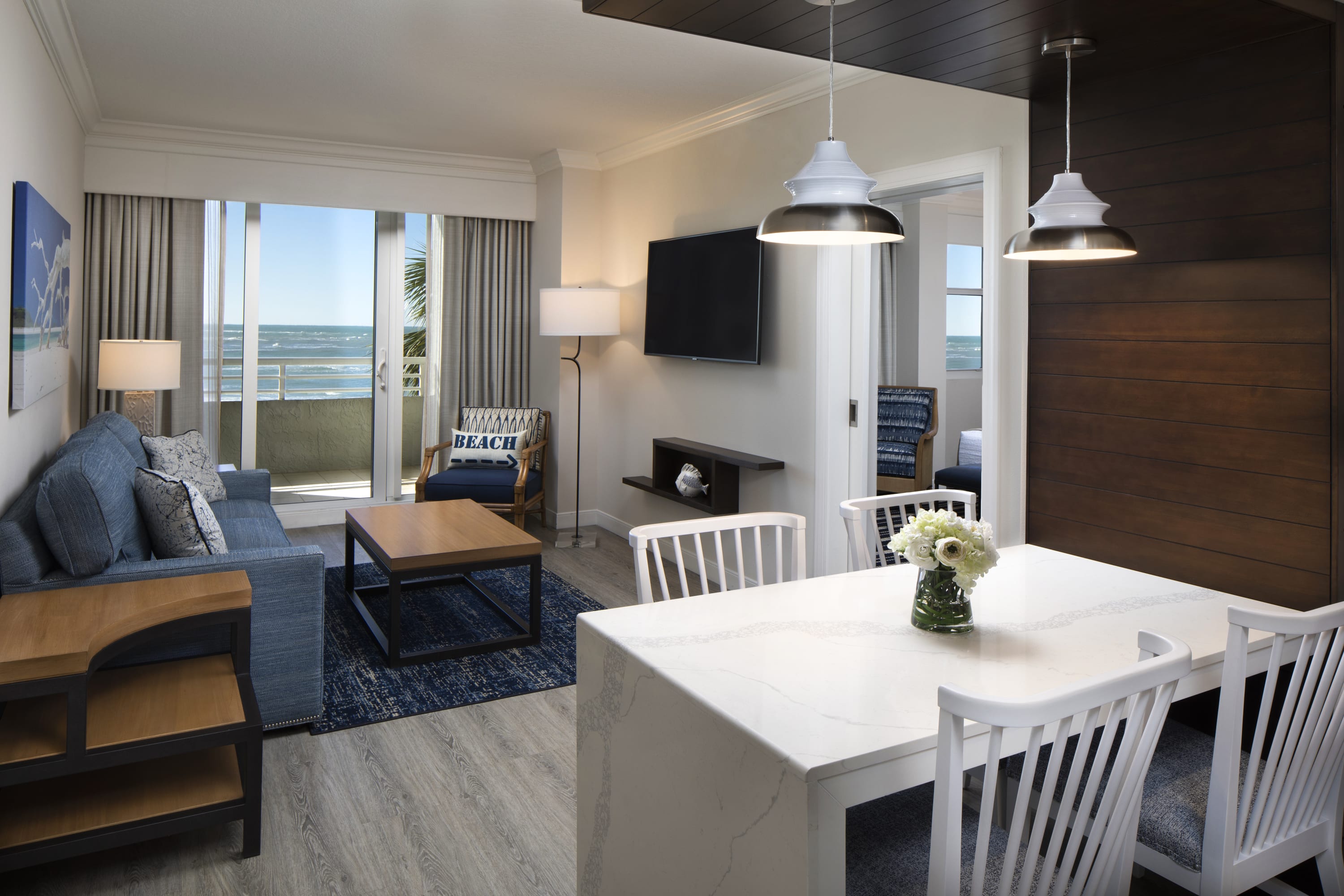 Living room and dining table looking out to an open sliding glass door with ocean view