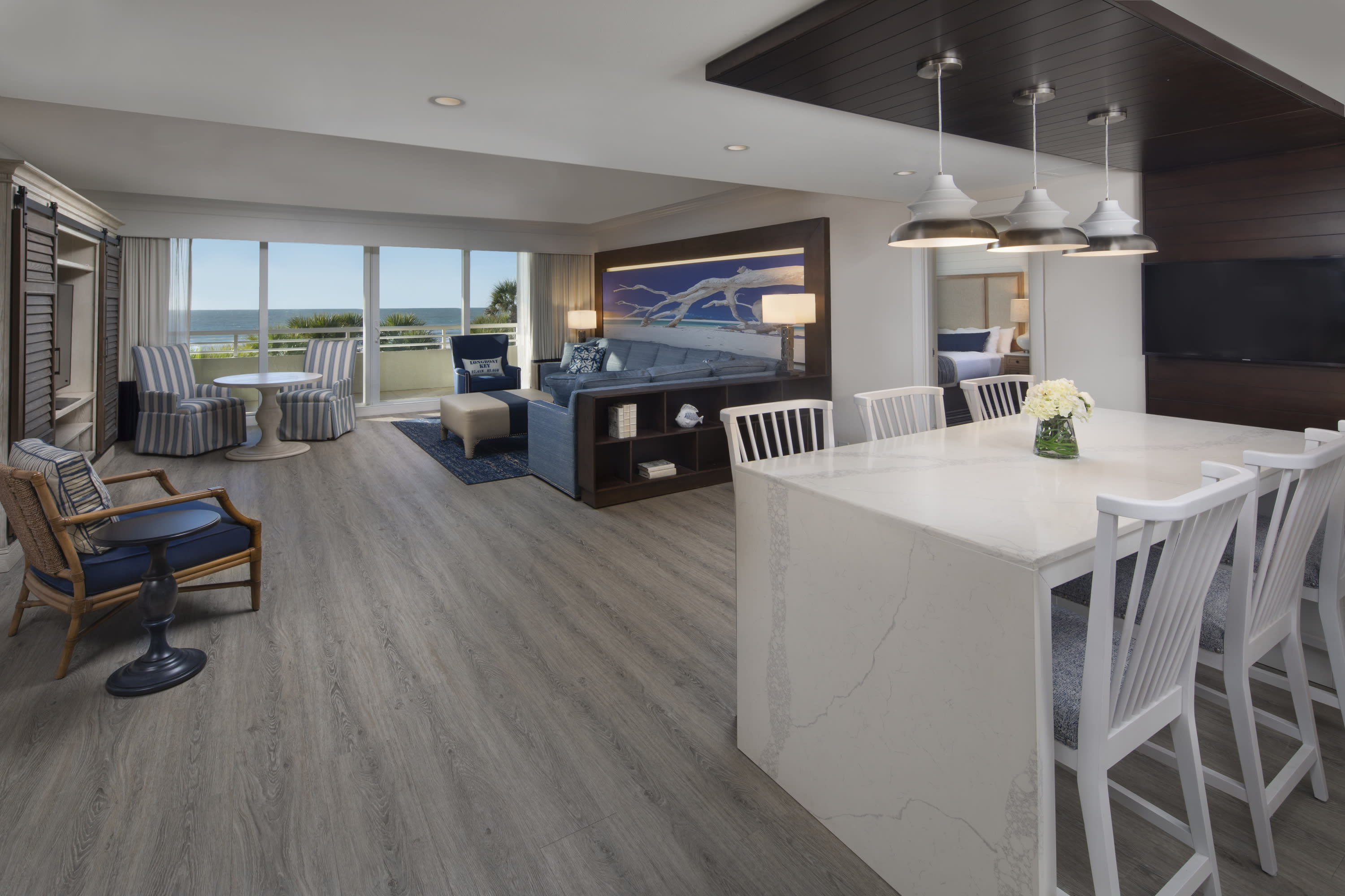 large living room with chairs and round tables, couch, mural on the wall, white dining table and chairs, and balcony overlook