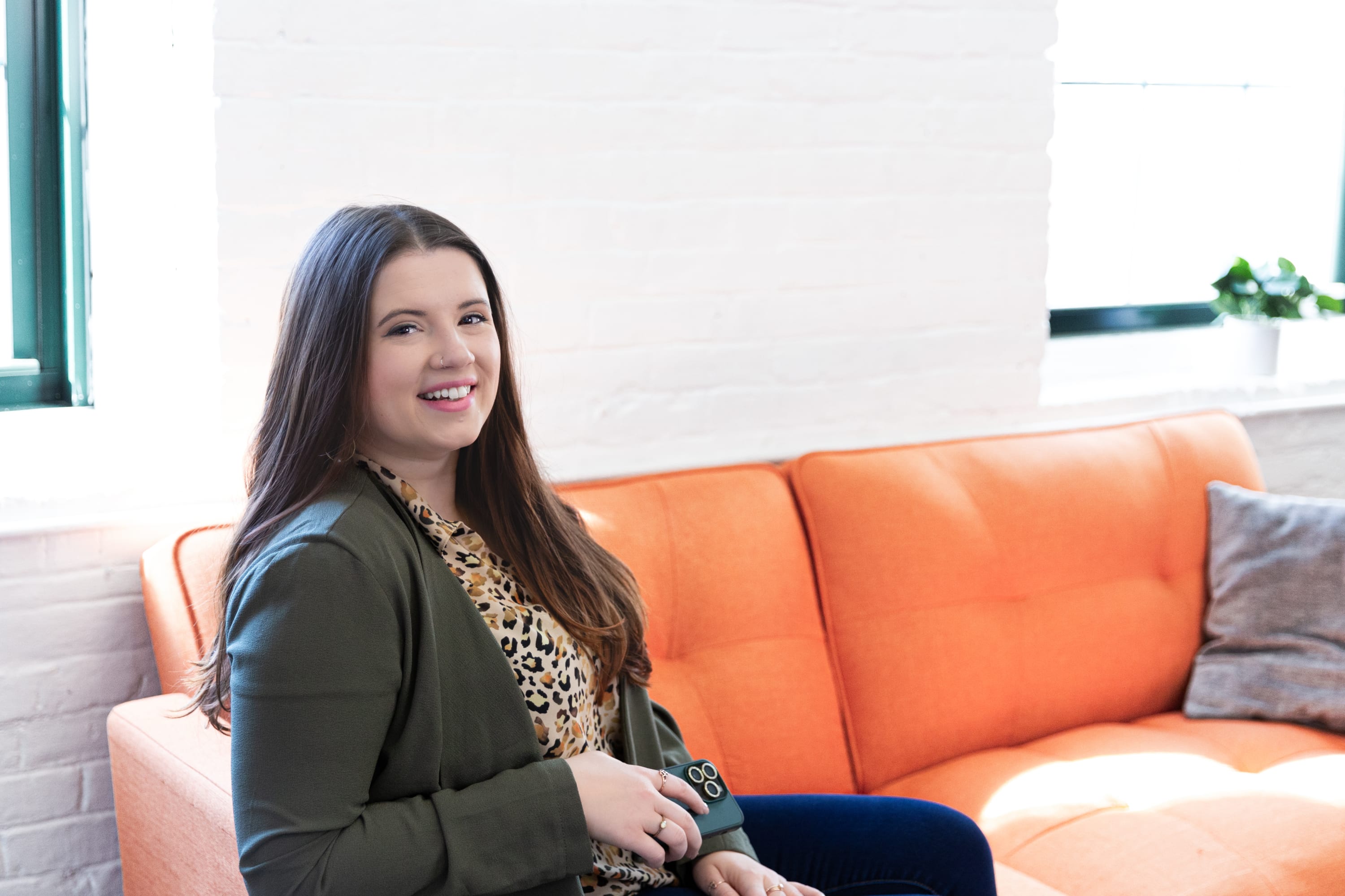 Photo of Leia Owen - Marketing & Business Consultant, LLC sitting on an orange couch and holding a phone for social media
