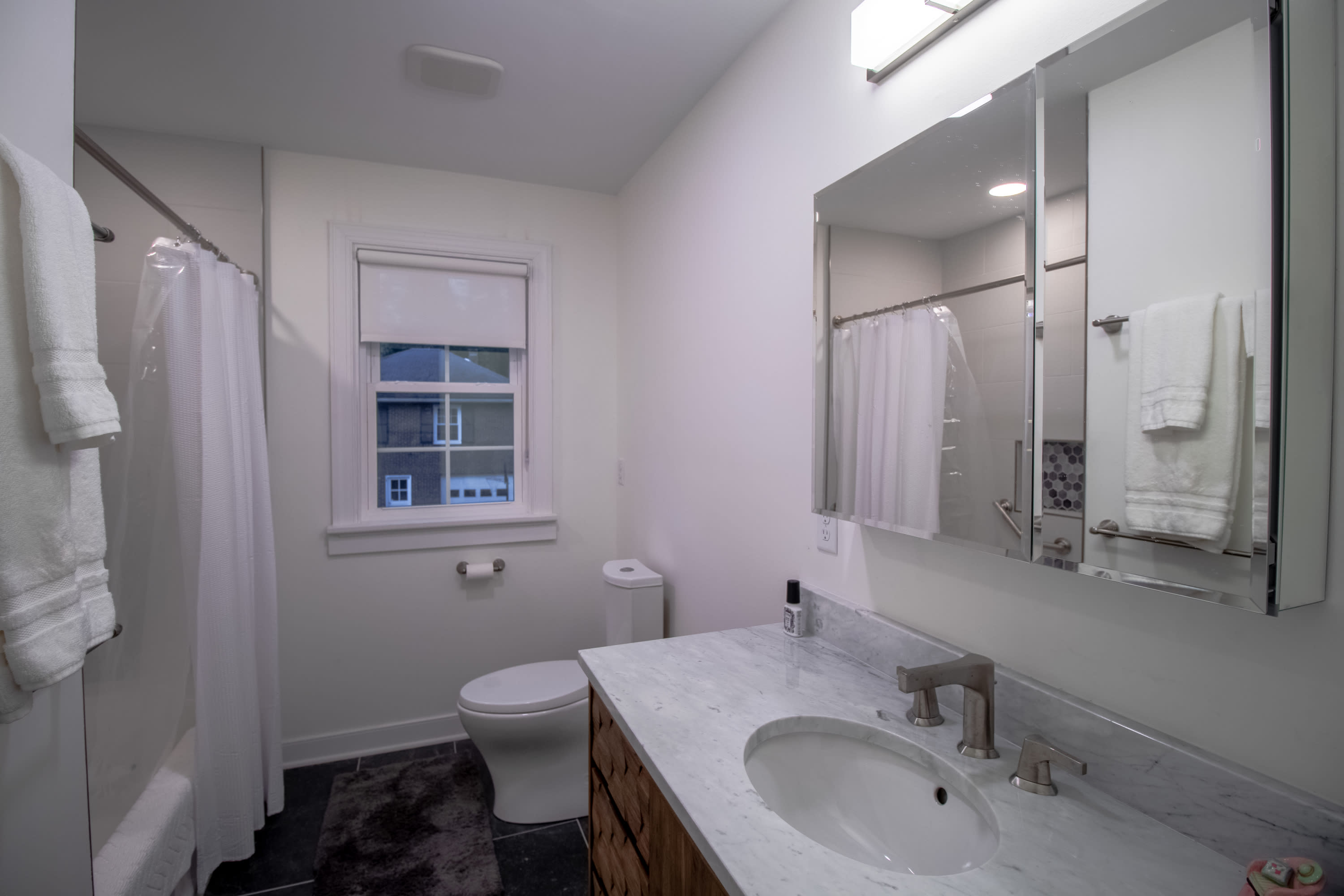 Modern hall bathroom with custom vanity, wall mirror cabinet, and white walls.