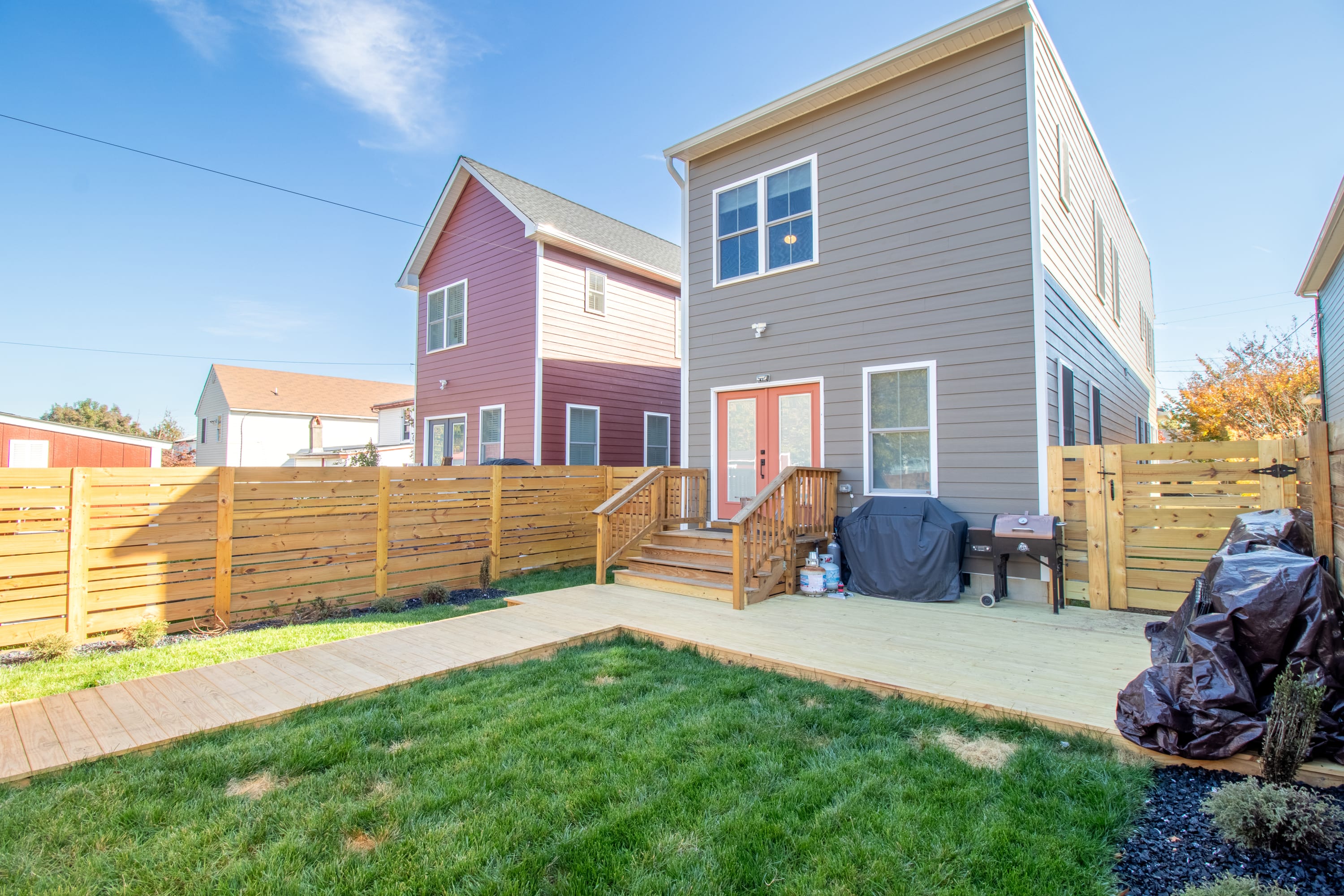 Wide view of completed backyard deck and wood fencing with green lawn.