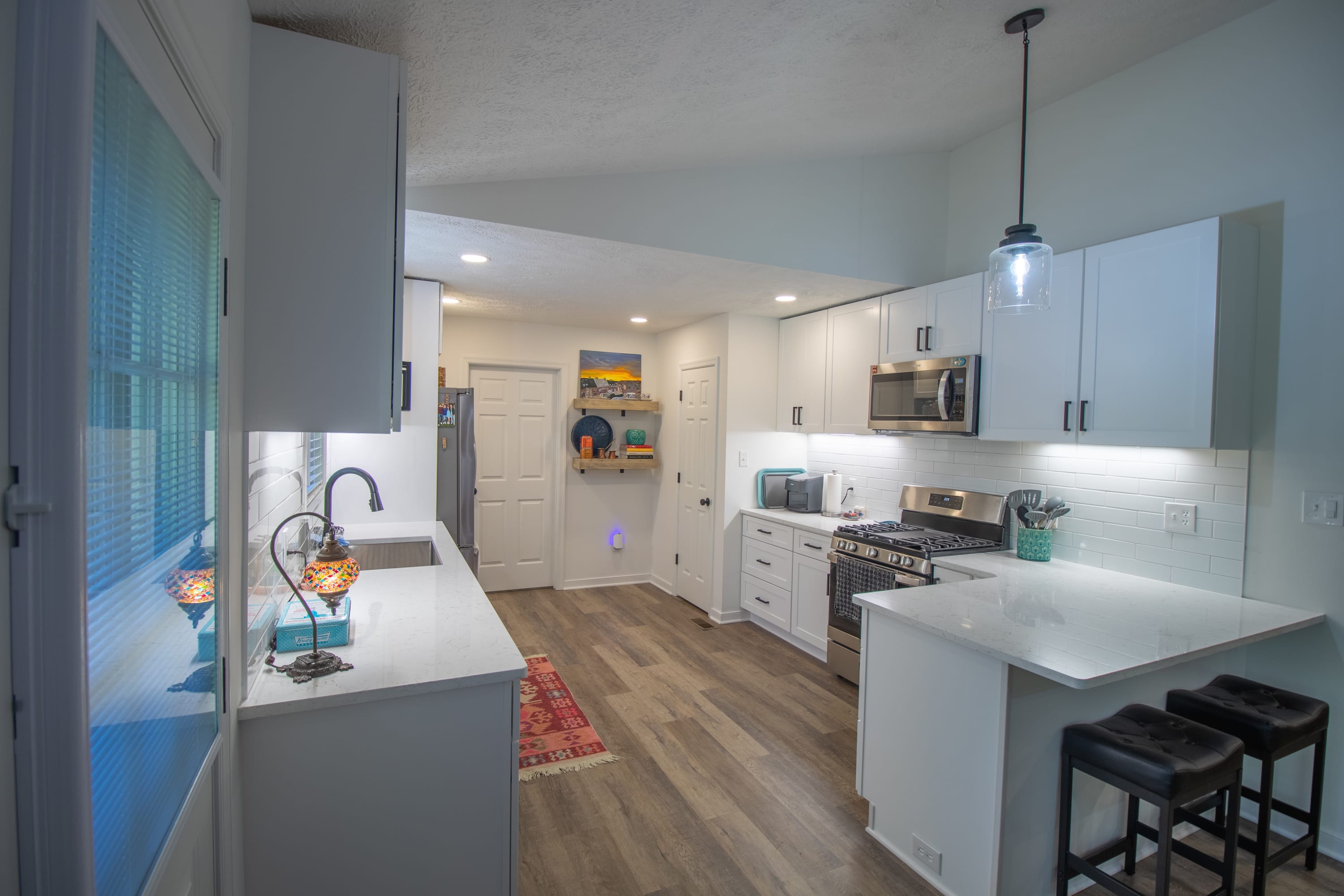 Open kitchen with breakfast bar, white cabinetry, subway tile backsplash, and modern lighting.