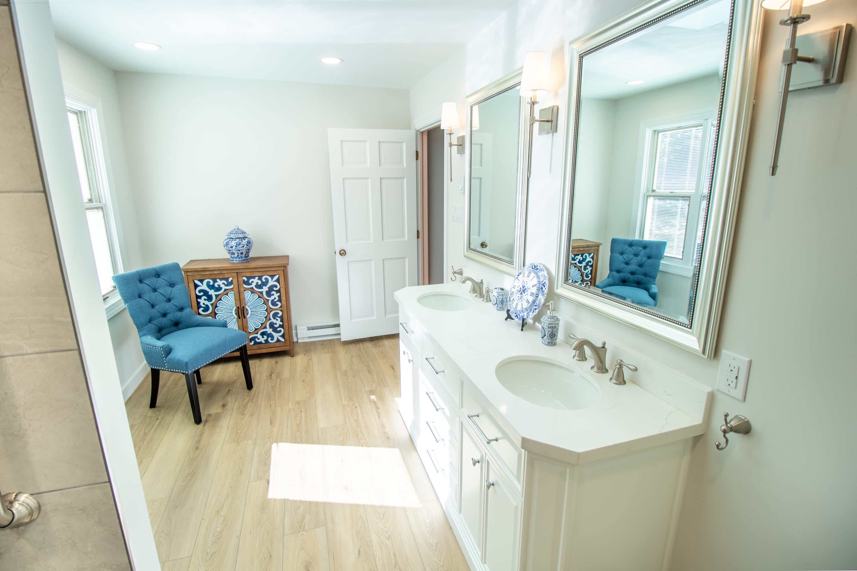 Bathroom with double vanity, decorative blue cabinet, and tufted accent chair.