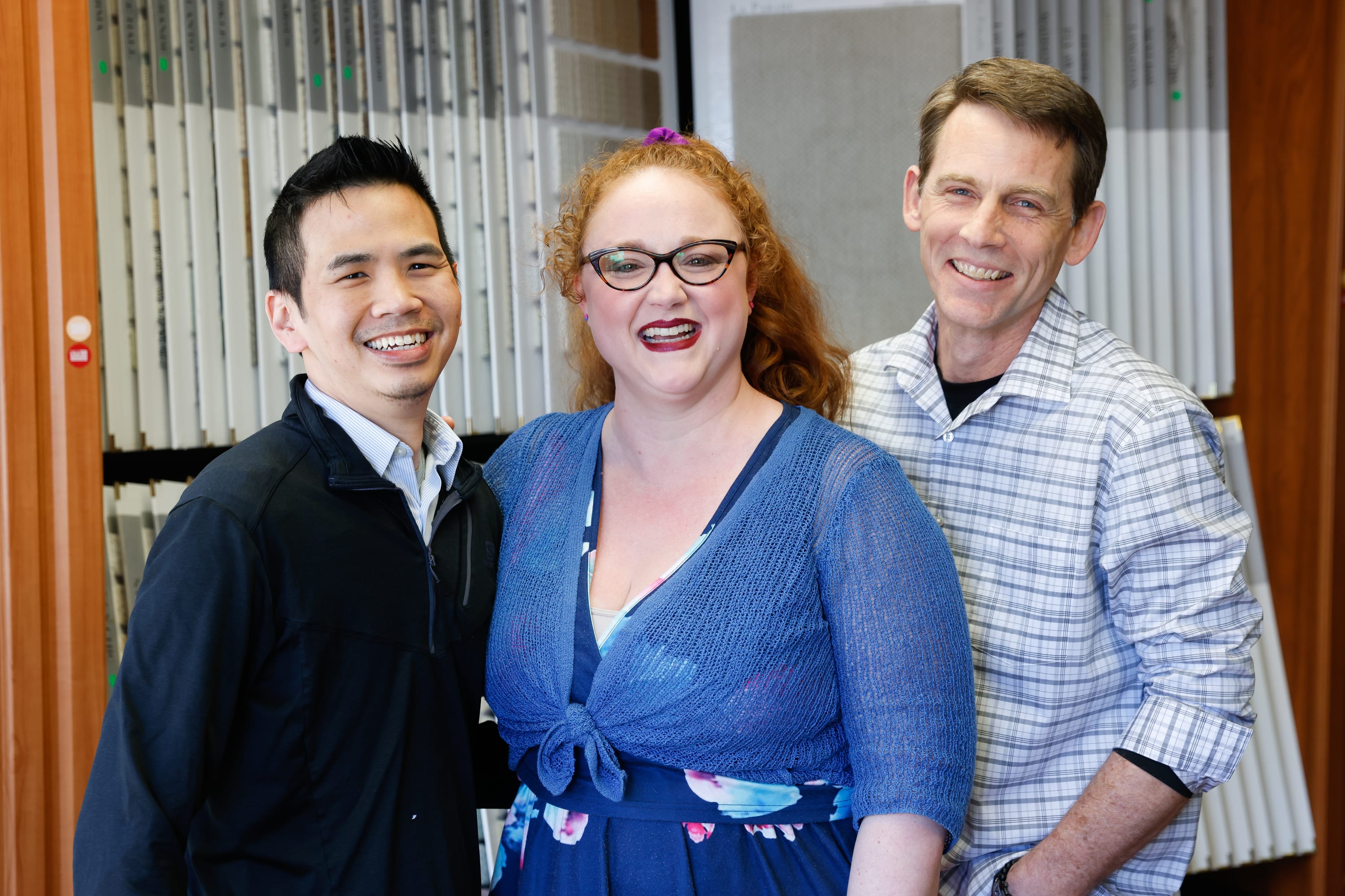 three smiling people posing together in front of a carpet display