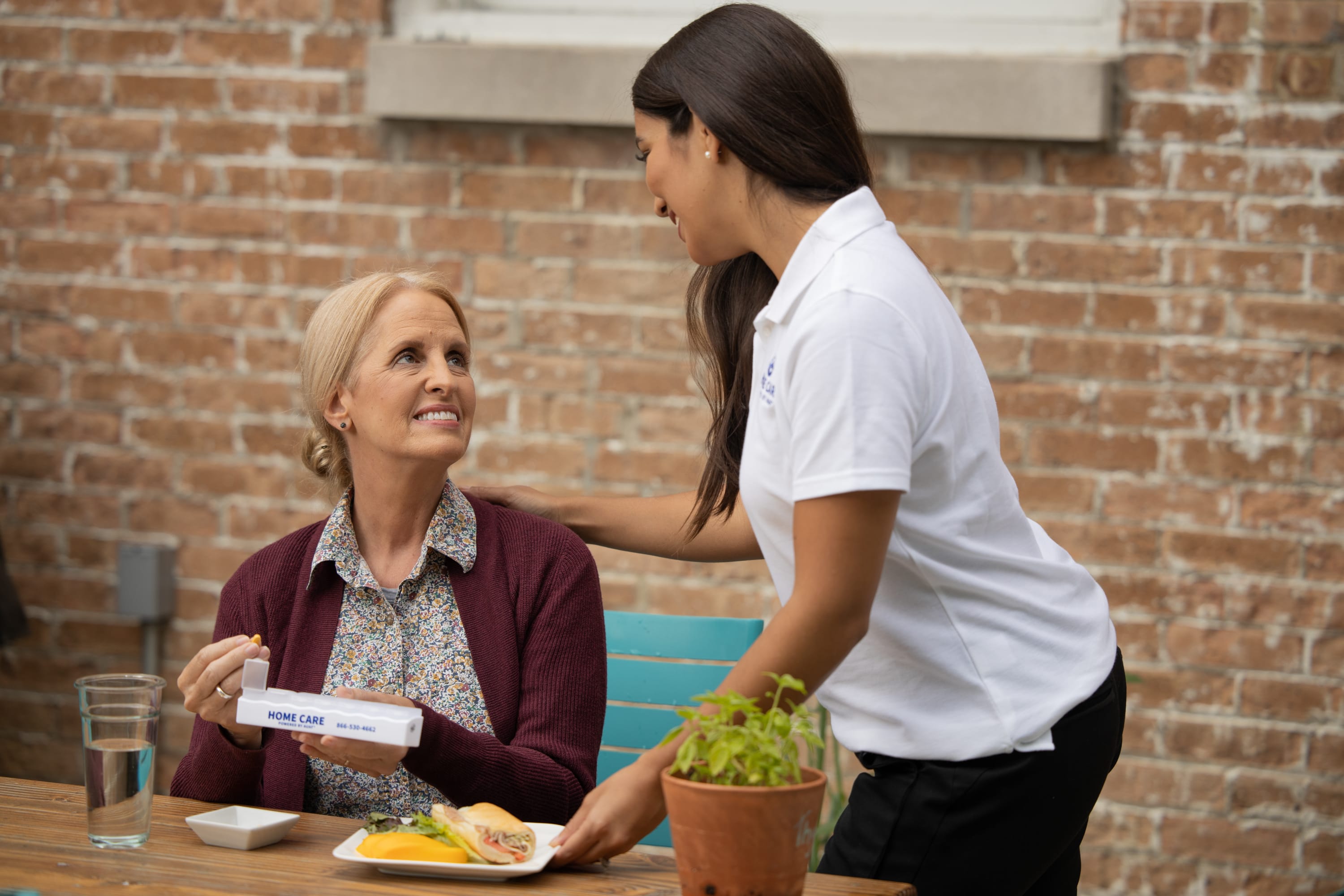 Caregiver serving lunch to elderly woman in his kitchen.