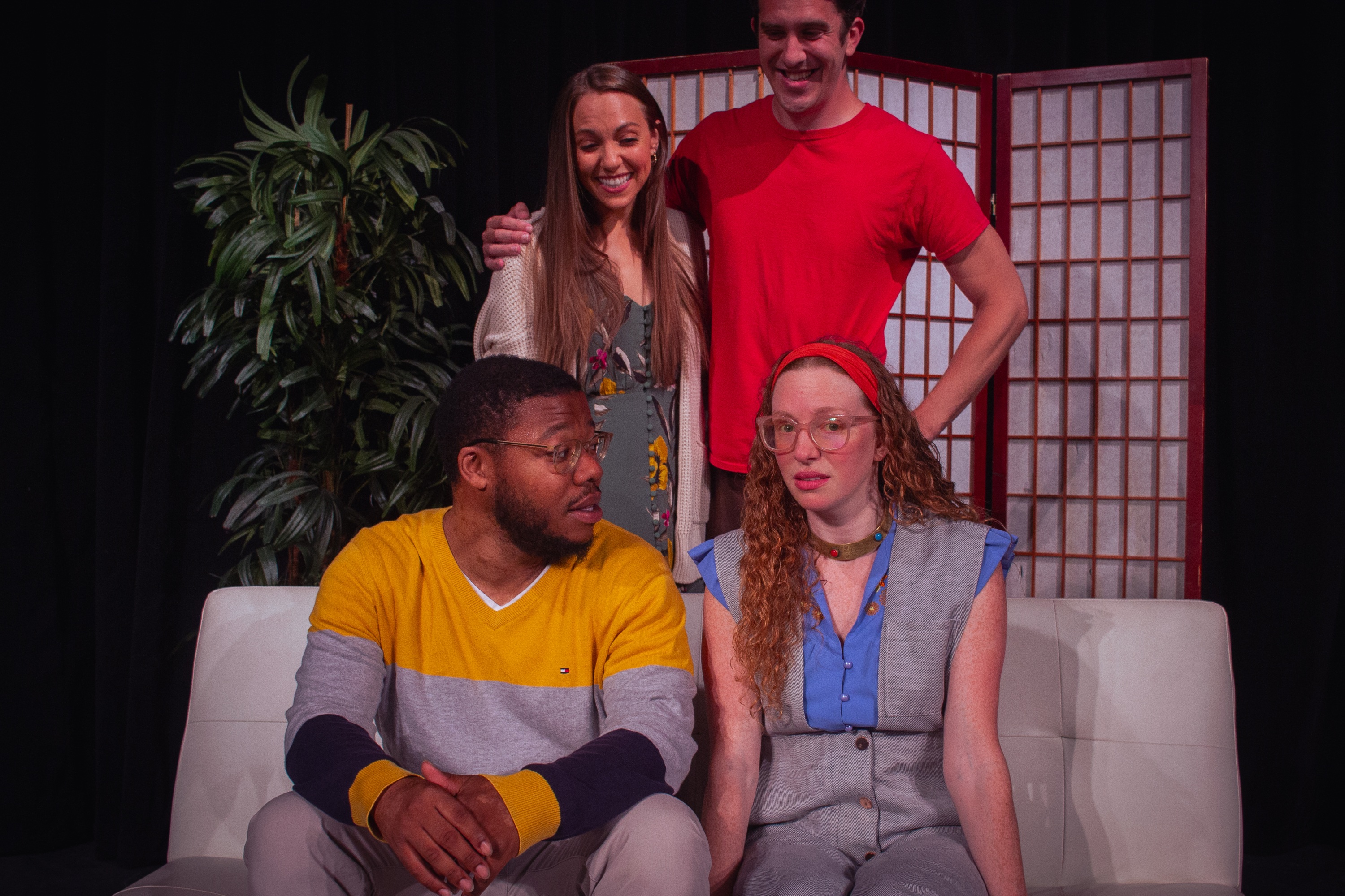 A couple in the background excitedly looking at their new friends (who are not as thrilled) sitting on the couch in front of
