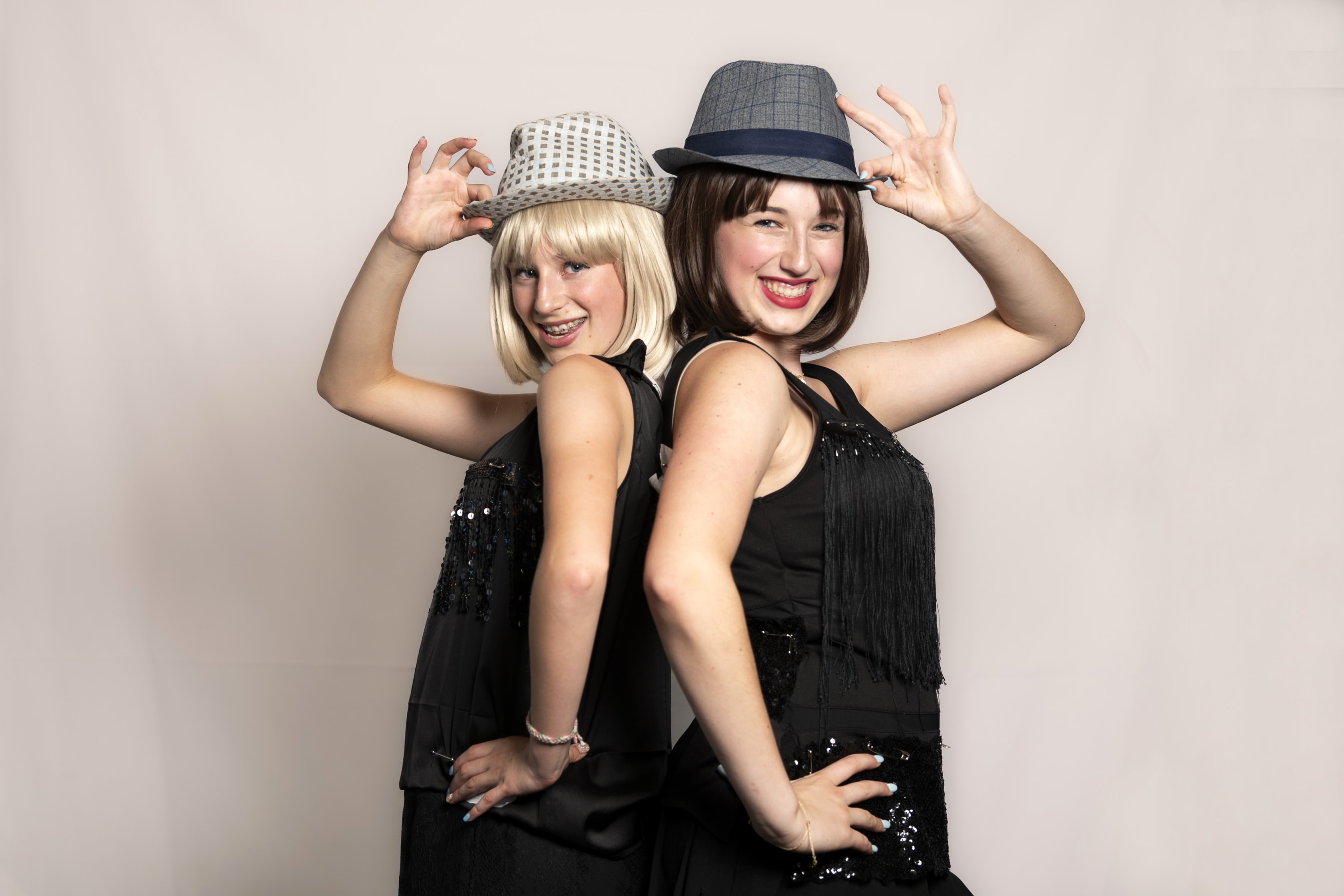 Two Chicago dancers in 20s-era hats posed back-to-back with one hand on their hip and another hand holding the brim of their