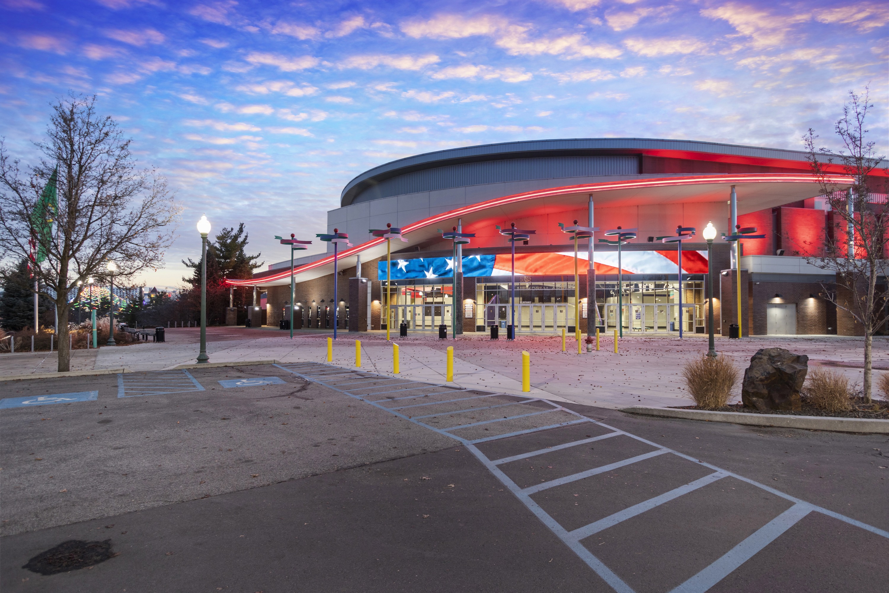 Dusk aerial photo of the arena with lights on and the parking lot in the foreground.