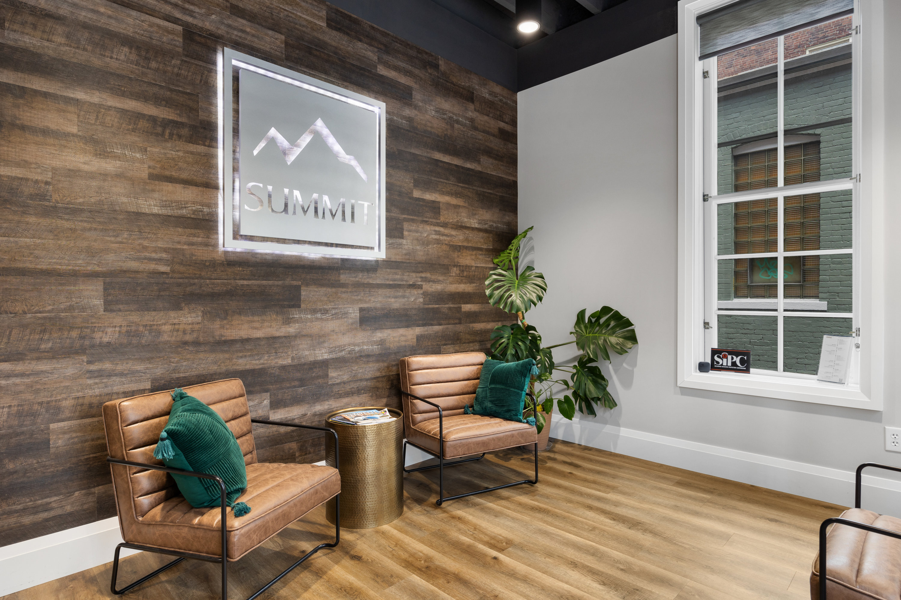 Lobby area with brown leather chairs, green pillows, a wooden accent wall with the Summit logo, and a large window.