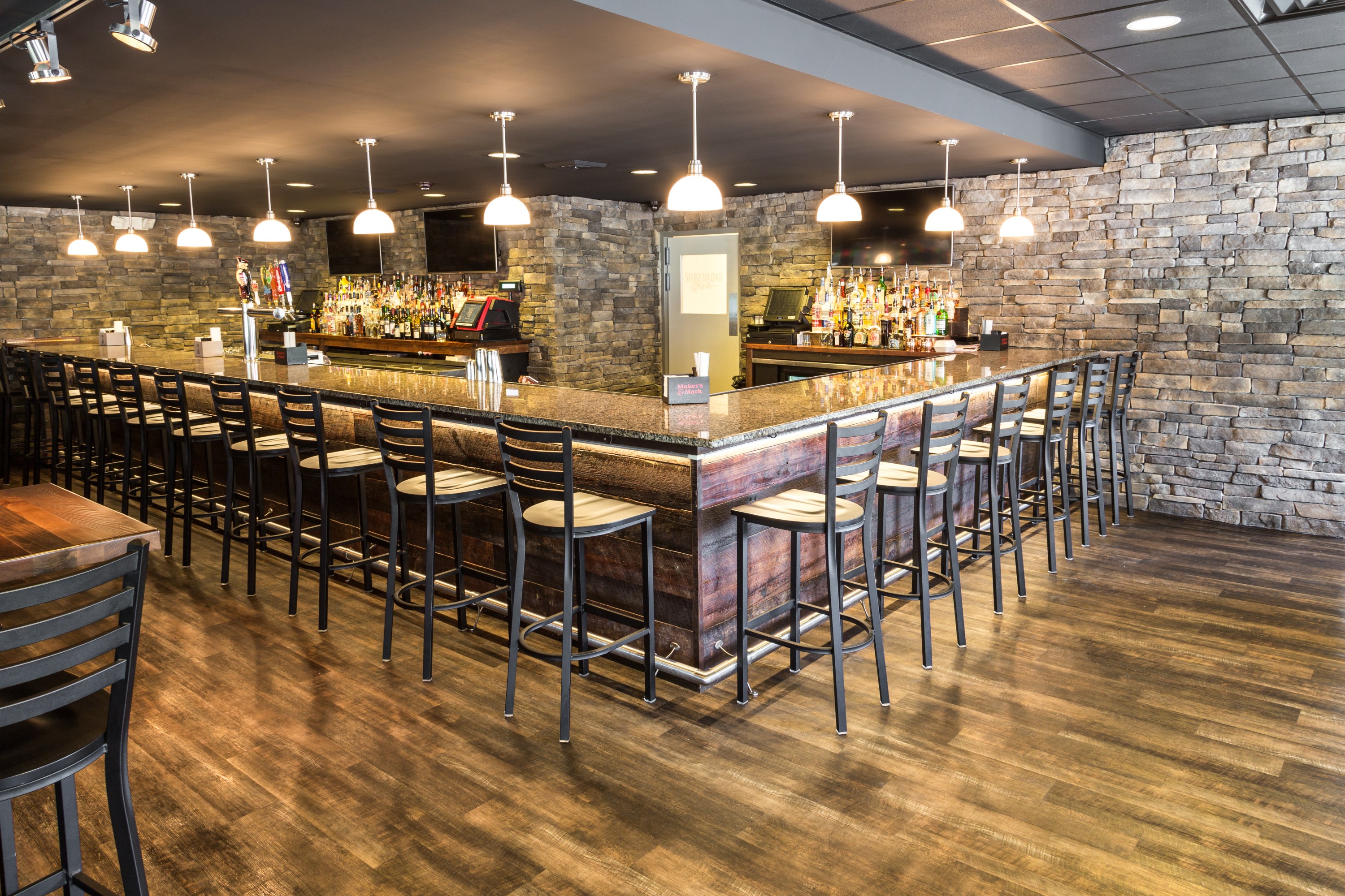 A large, modern bar area featuring a long L-shaped bar with a dark wood base, granite countertop