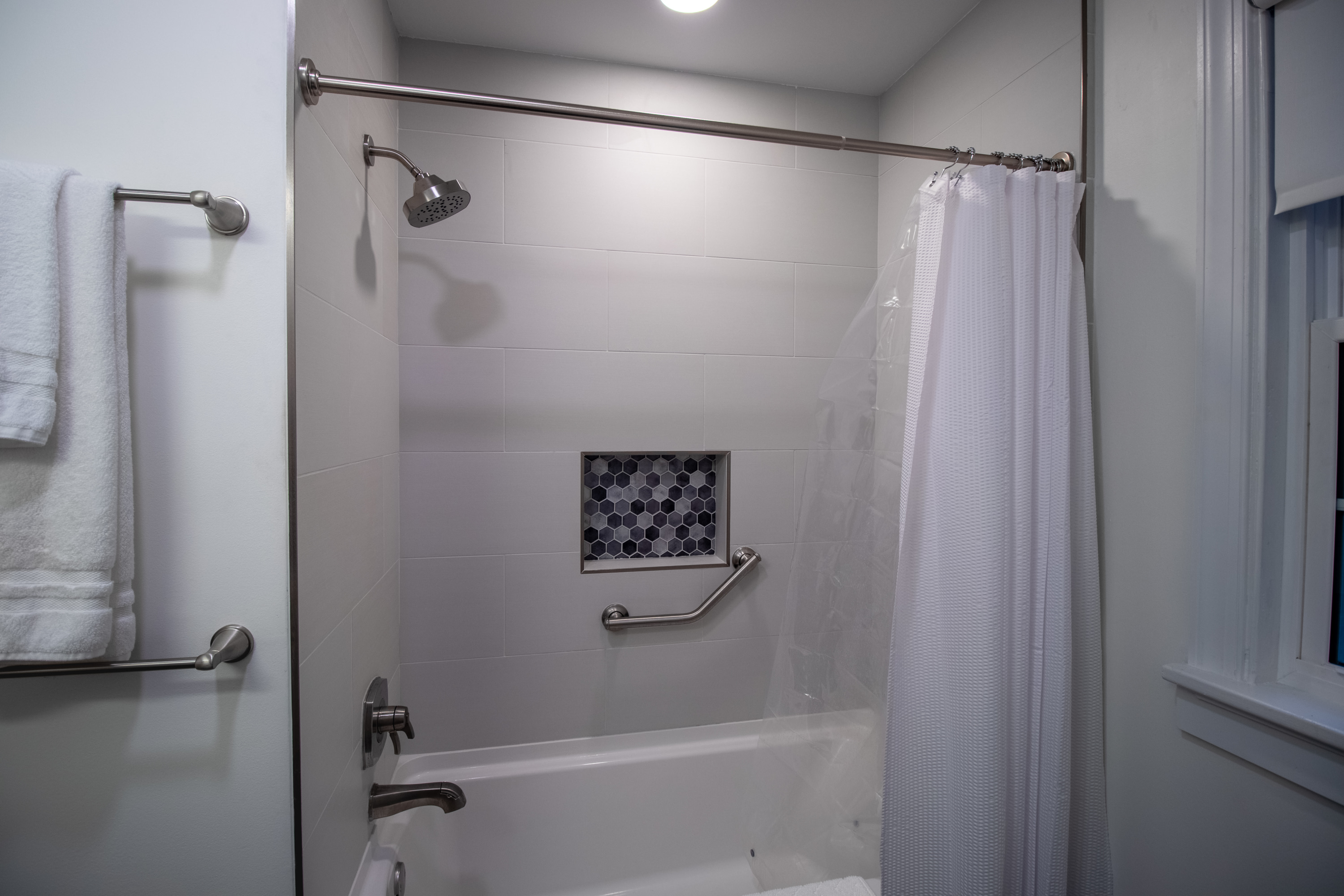 Tub and shower combo with white tile walls, chrome fixtures, and a hexagon tile niche.