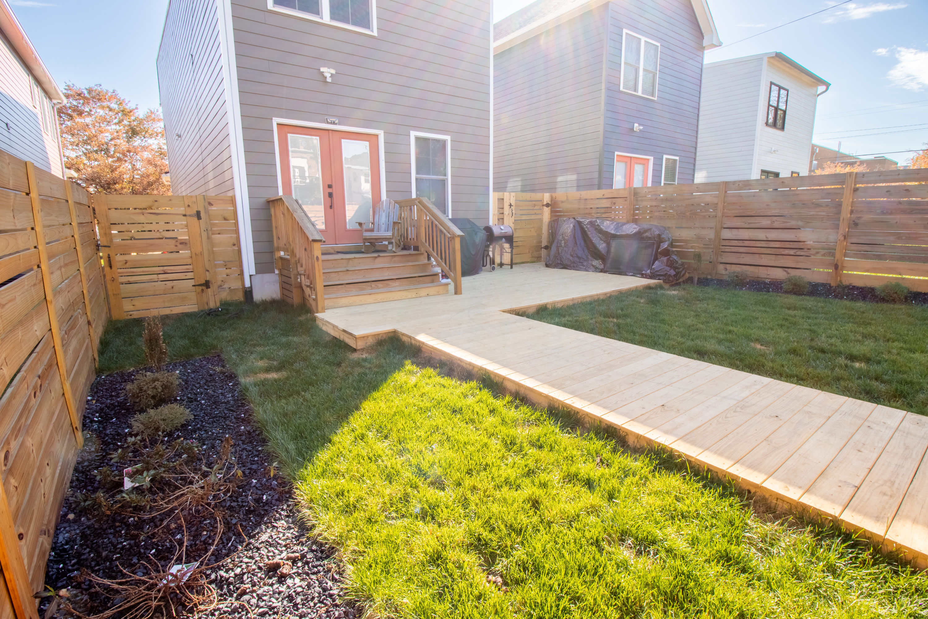 Side view of backyard deck, wooden walkway, and landscaped garden beds.