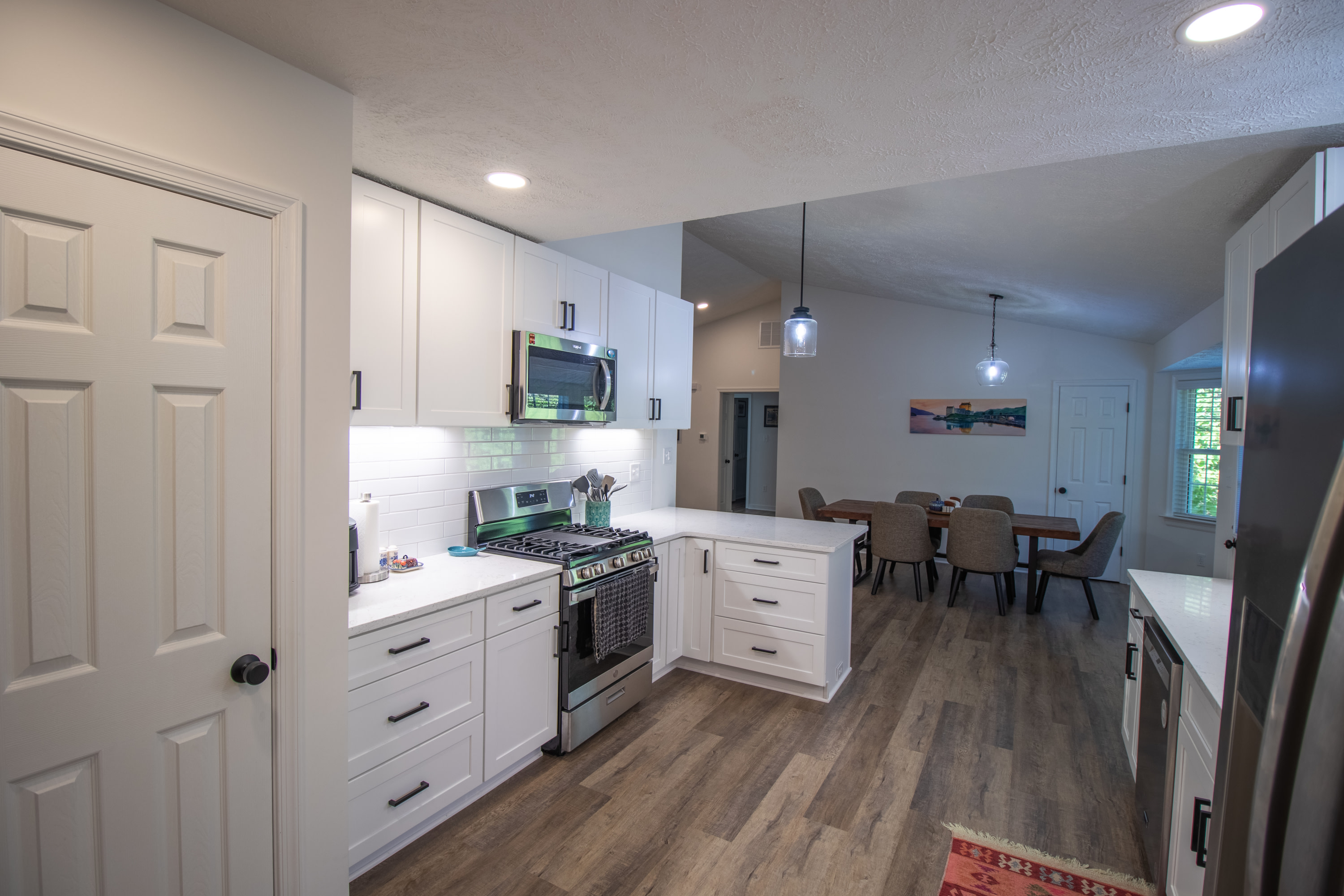 Kitchen with stainless steel range and microwave, leading to open dining room.